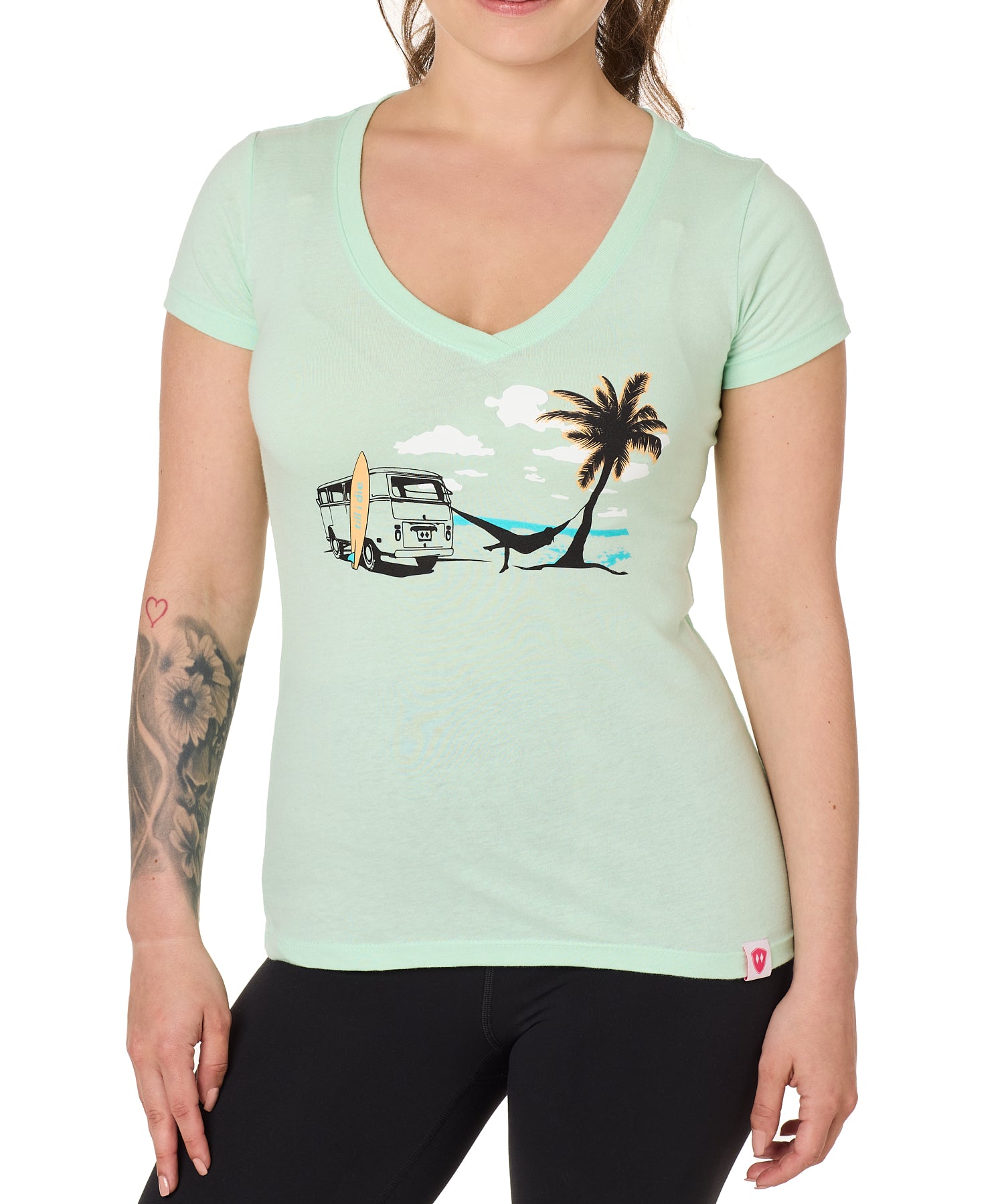 Front view of a female model wearing the Hammock V-neck tee in mint, displayed on a white background. The graphic depicts a vintage VW bus parked on a beach, with a surfboard leaning against it and a silhouetted figure relaxing in a hammock strung between the van and a palm tree.