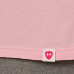 Close-up detail of a pink Double Diamond Shield woven hem label on a light pink crew neck tee.