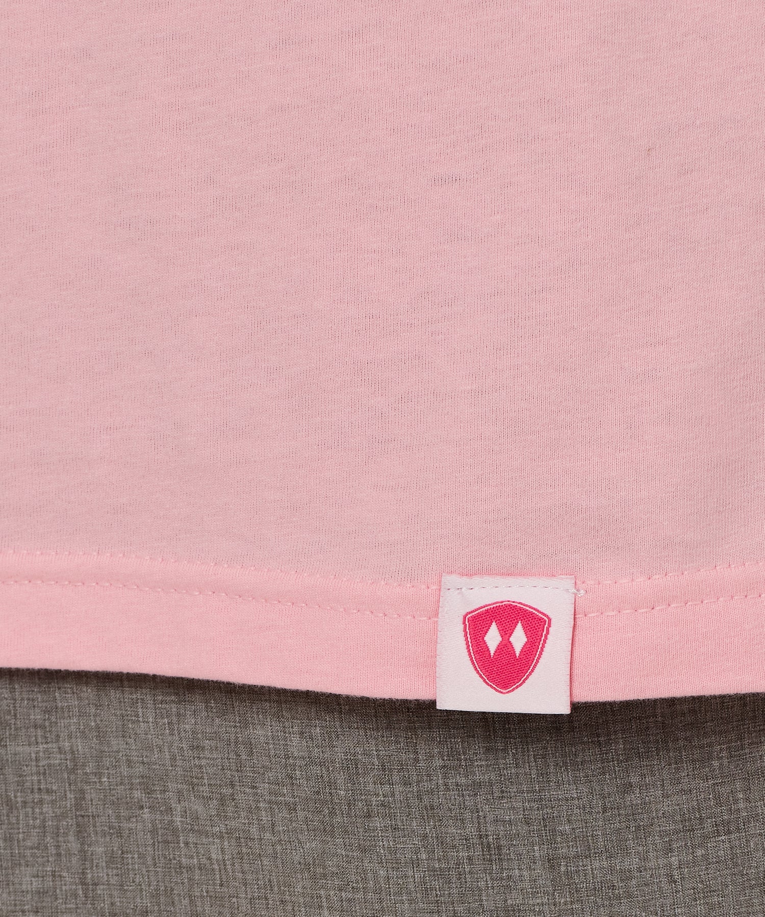 Close-up detail of a pink Double Diamond Shield woven hem label on a light pink crew neck tee.