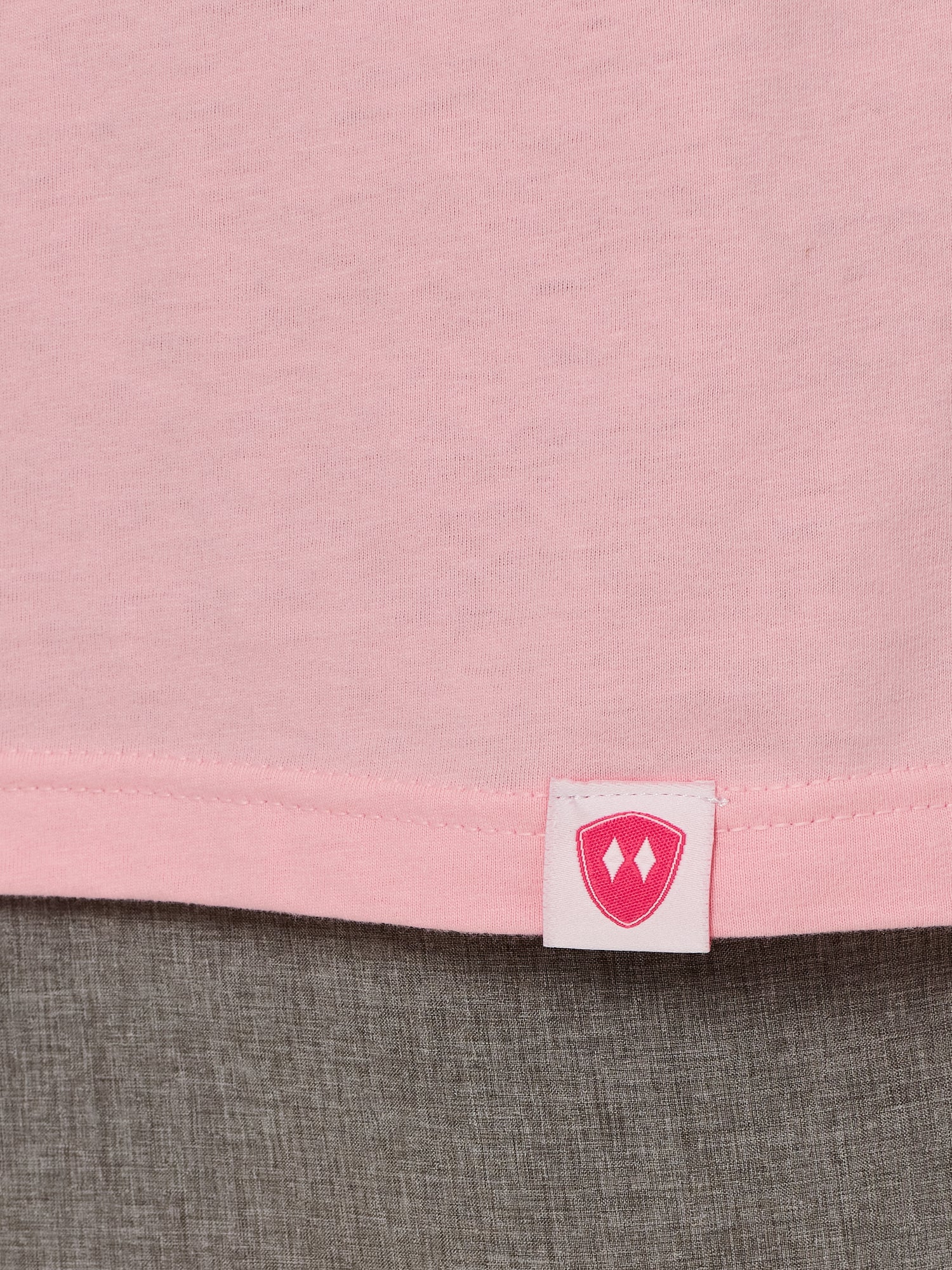 Close-up detail of a pink Double Diamond Shield woven hem label on a light pink crew neck tee.
