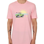 Front view of a male model wearing the Surf Truck crew neck tee in light pink on a white background. The graphic features a classic green Bronco with a surfboard on the roof, parked in front of an ocean sunset, arched by “Till I Die” text.