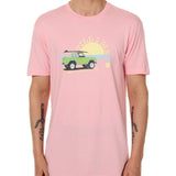 Front view of a male model wearing the Surf Truck crew neck tee in light pink on a white background. The graphic features a classic green Bronco with a surfboard on the roof, parked in front of an ocean sunset, arched by “Till I Die” text.
