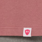 Close-up detail of a pink Double Diamond Shield woven hem label on a deep sunset long sleeve shirt.
