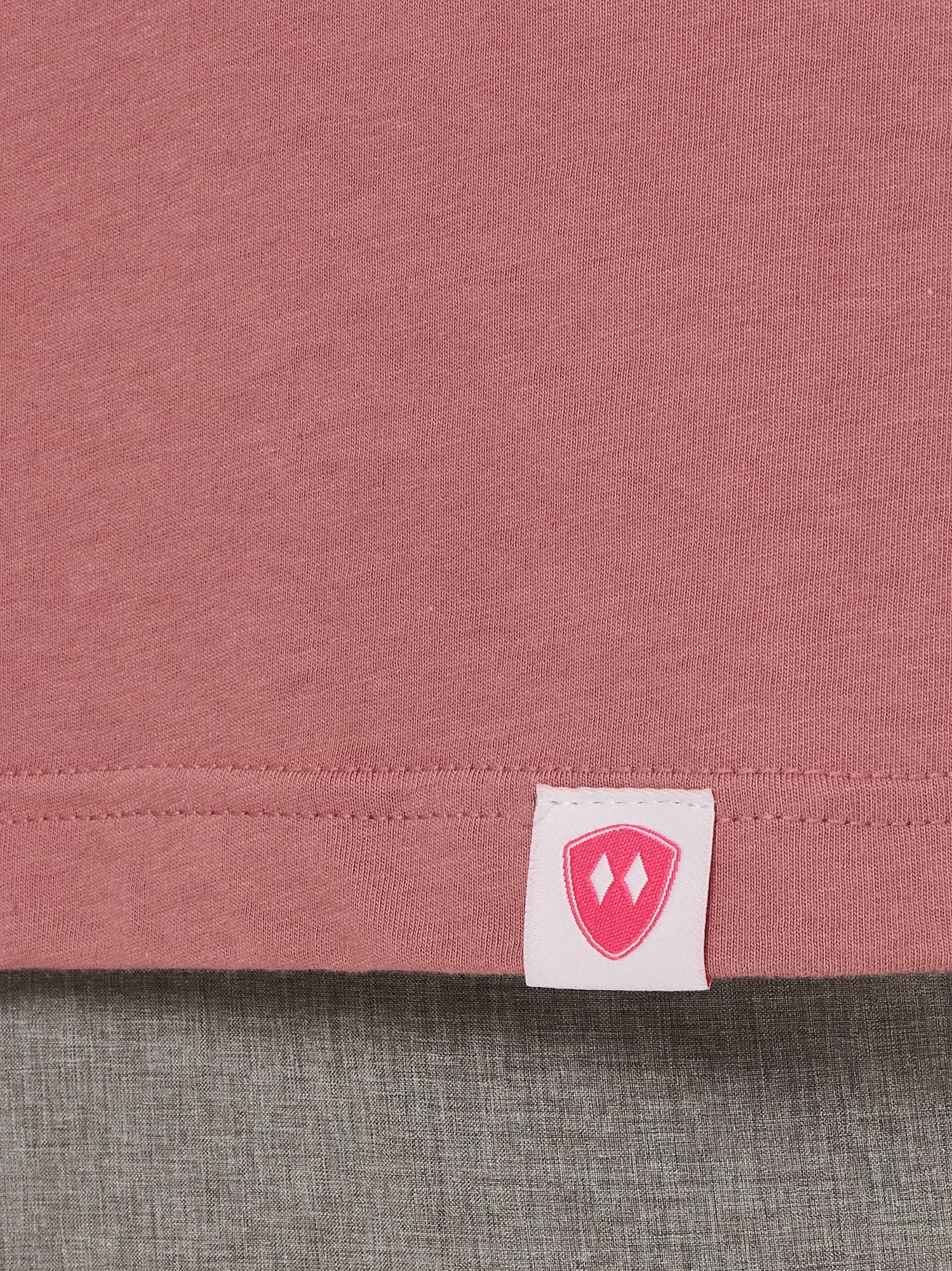 Close-up detail of a pink Double Diamond Shield woven hem label on a deep sunset long sleeve shirt.