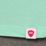 Close-up detail of a pink Double Diamond Shield woven hem label on a mint green shirt.