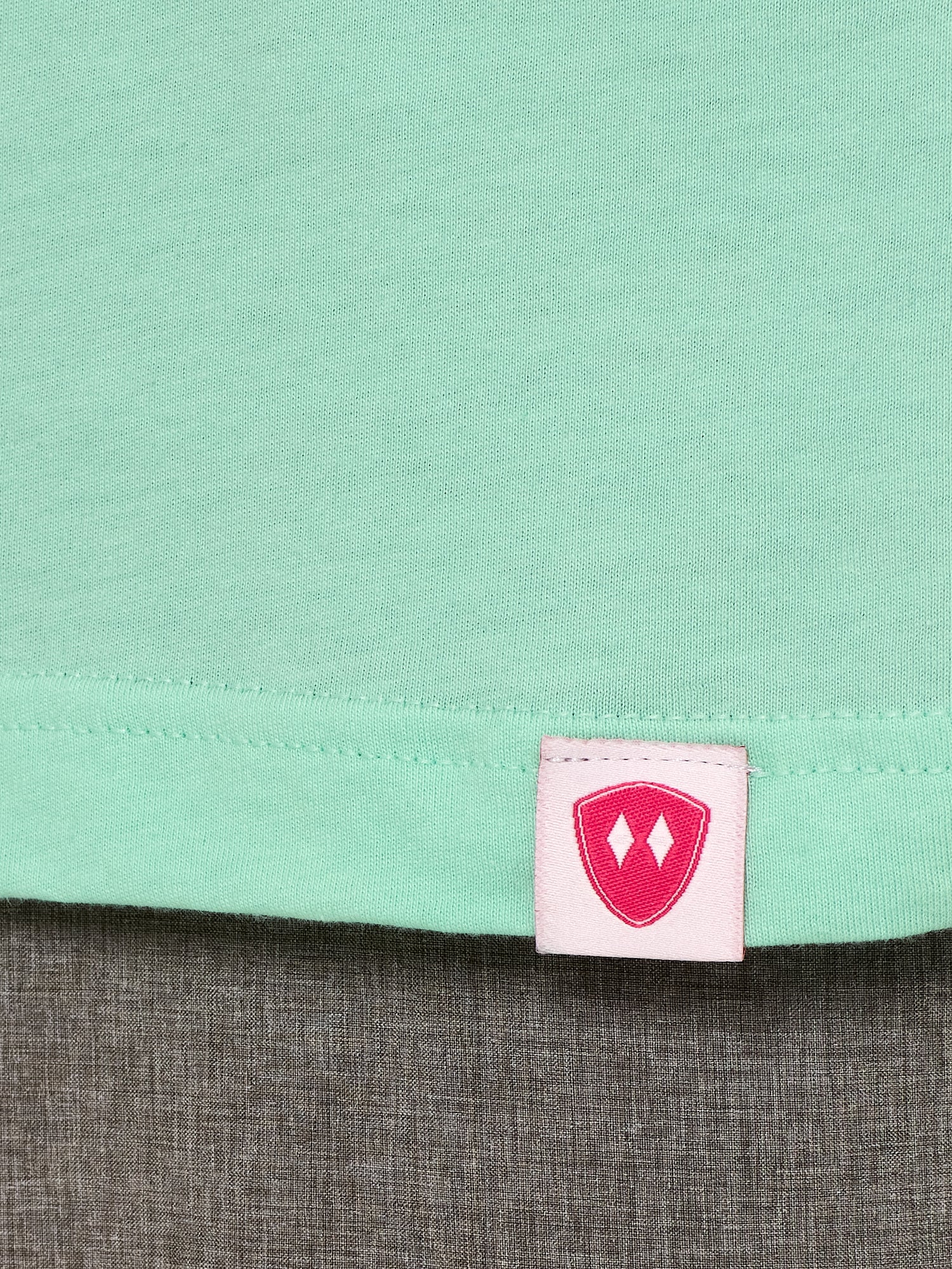 Close-up detail of a pink Double Diamond Shield woven hem label on a mint green shirt.