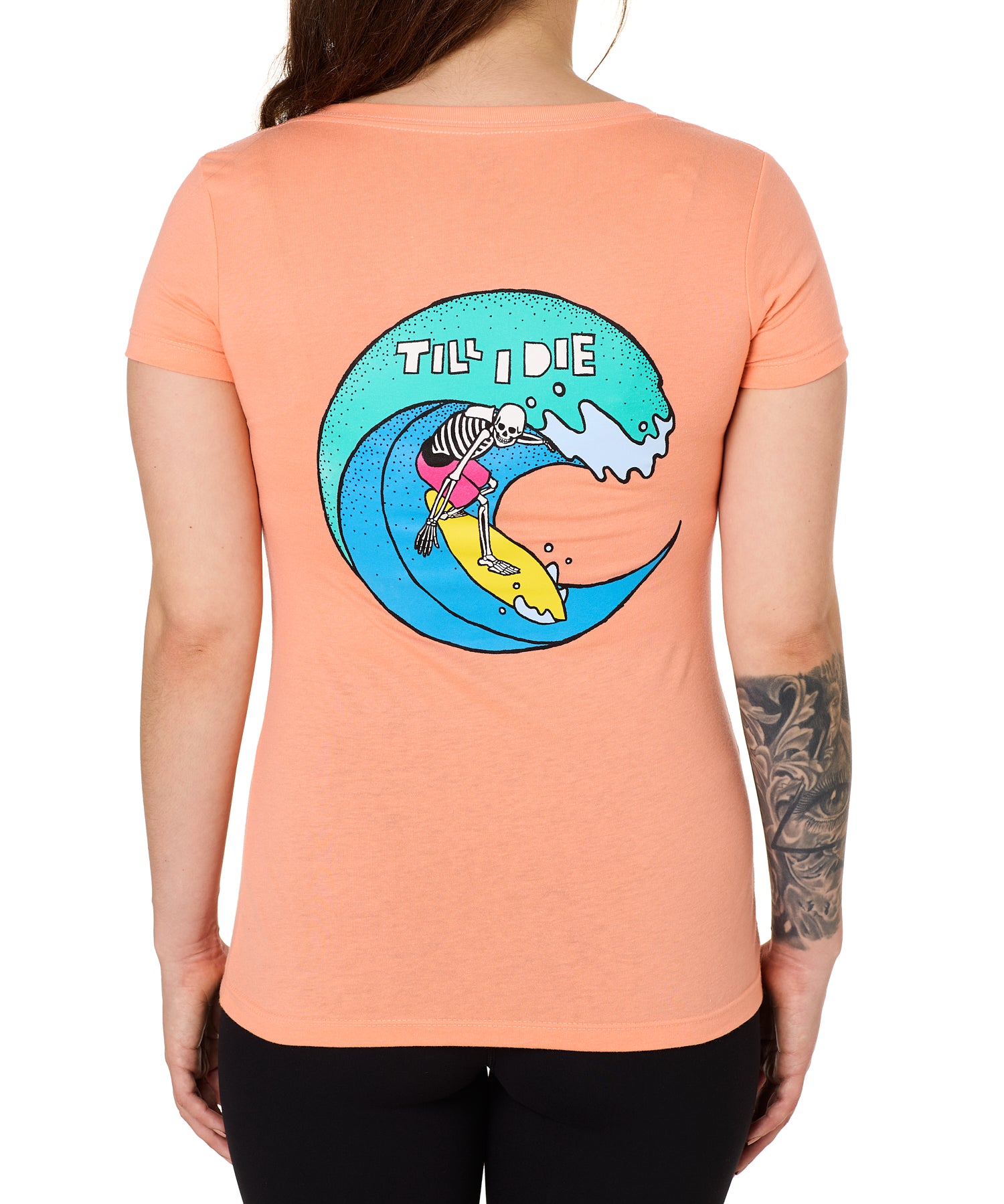 Back view of a female model wearing the Surfer Skeleton tee in citrus on a white background. The graphic features a multicolored circular graphic of a skeleton surfing a wave, with “Till I Die” text at the top.