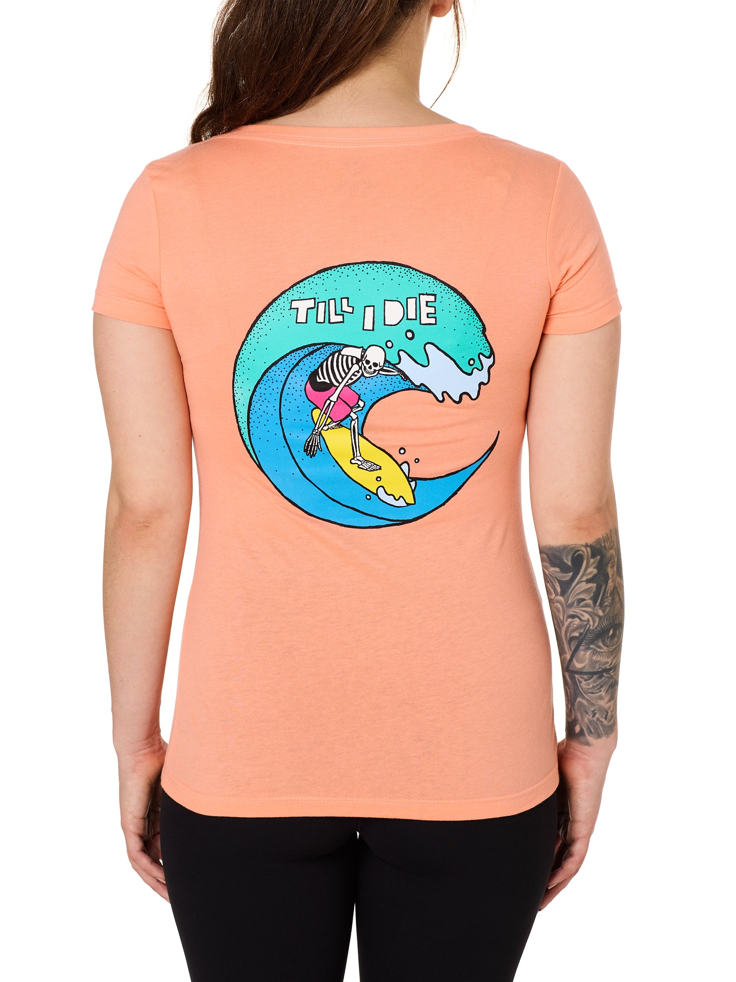 Back view of a female model wearing the Surfer Skeleton tee in citrus on a white background. The graphic features a multicolored circular graphic of a skeleton surfing a wave, with “Till I Die” text at the top.