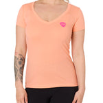 Front view of a female model wearing the Surfer Skeleton V neck tee in citrus on a white background. Accented with a hot pink double diamond shield over wearers left chest.