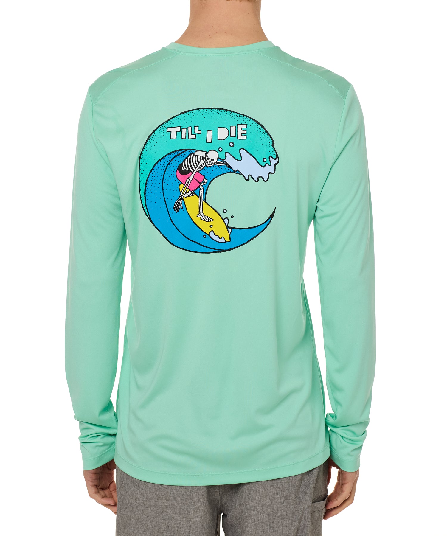 Back view of a male model wearing the Surfer Skeleton performance long sleeve tee in mint green on a white background. The graphic features a multicolored circular graphic of a skeleton surfing a wave, with “Till I Die” text at the top.