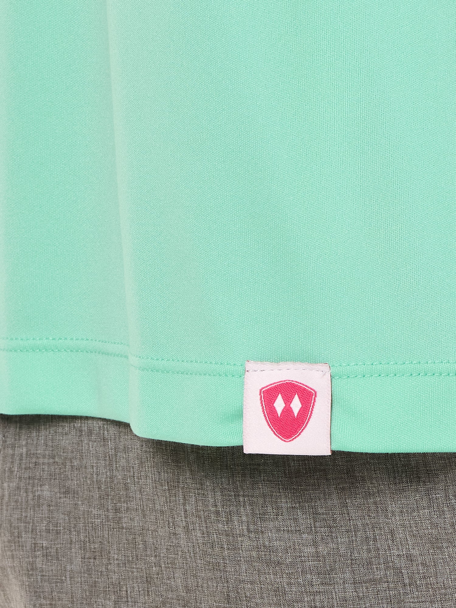 Close-up detail of a pink Double Diamond Shield woven hem label on a mint green performance long sleeve shirt.