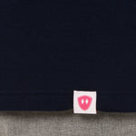 Close-up detail of a pink Double Diamond Shield woven hem label on a navy blue  shirt.