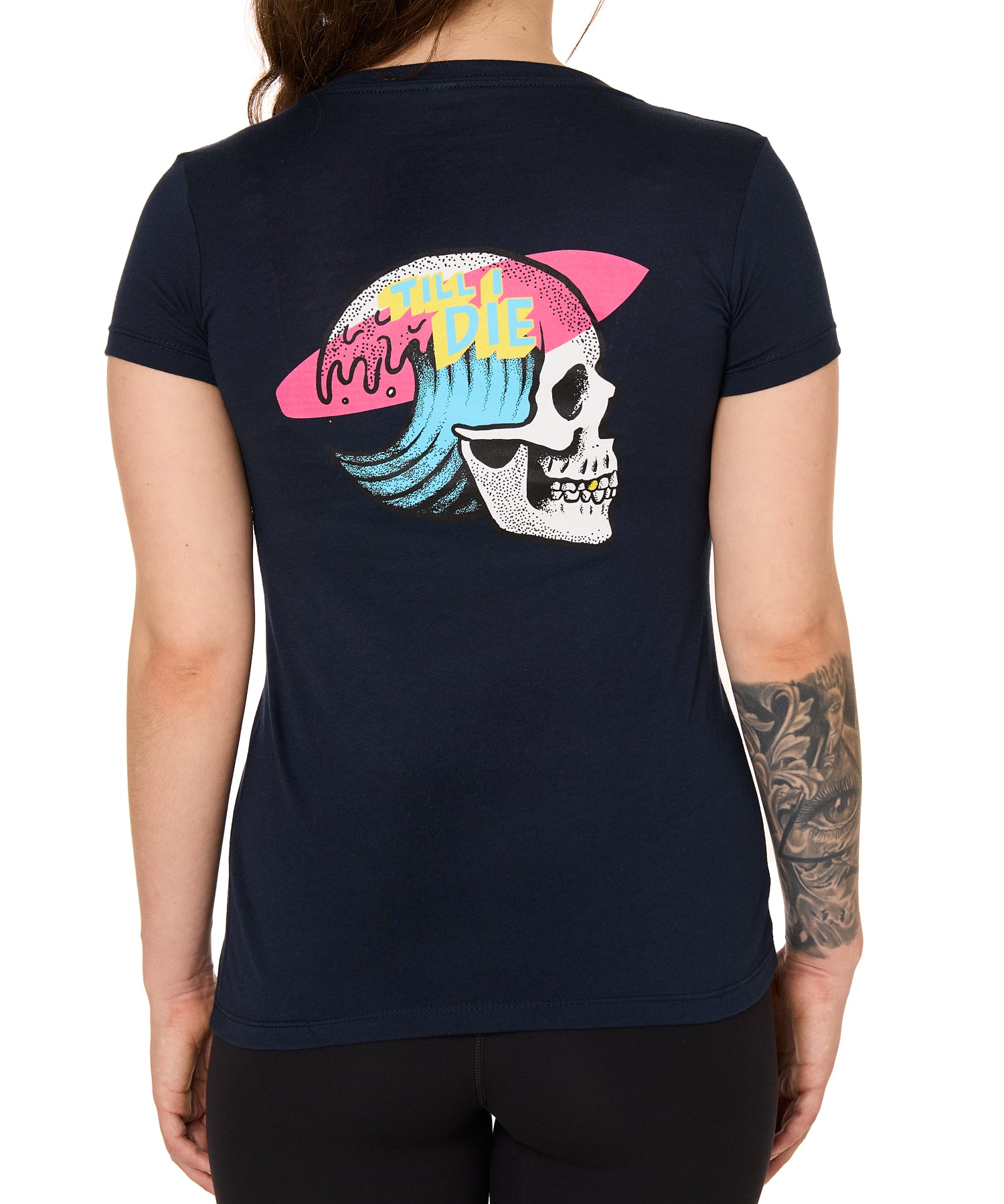 Back view of a female model wearing the Skull Wave Head Tee in navy. The back graphic features a skull with a wave inside the head, overlapped by a pink surfboard and accented with yellow and blue "Till I Die" text.