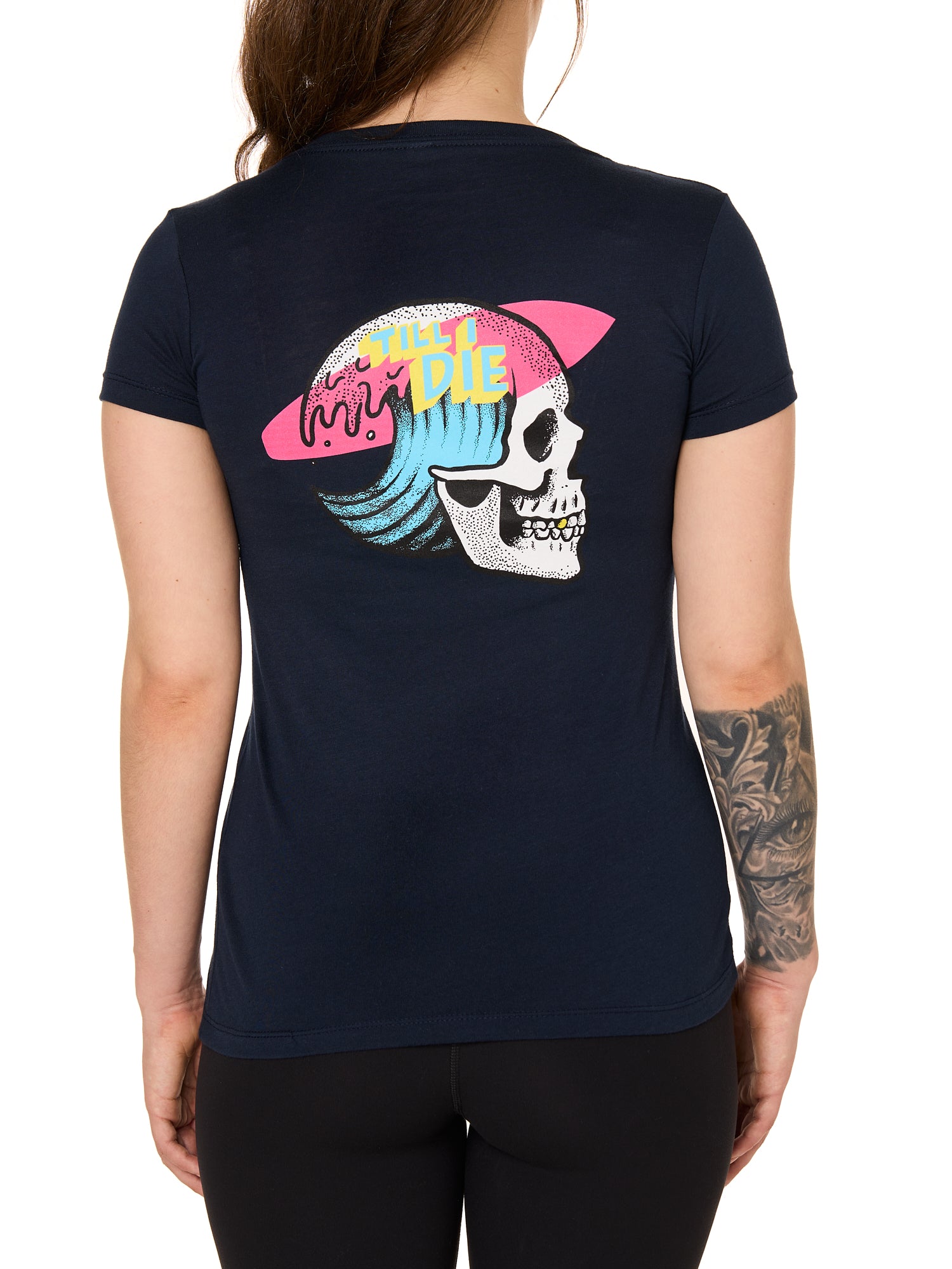 Back view of a female model wearing the Skull Wave Head Tee in navy. The back graphic features a skull with a wave inside the head, overlapped by a pink surfboard and accented with yellow and blue "Till I Die" text.