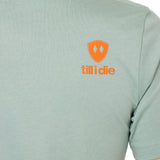 Back view of a male model wearing a Dusty blue short sleeve shirt on a white background, featuring an orange Till I Die logo on the wearer’s top right shoulder.
