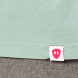 Close-up detail of a pink Double Diamond Shield woven hem label on a dusty blue short sleeve shirt.