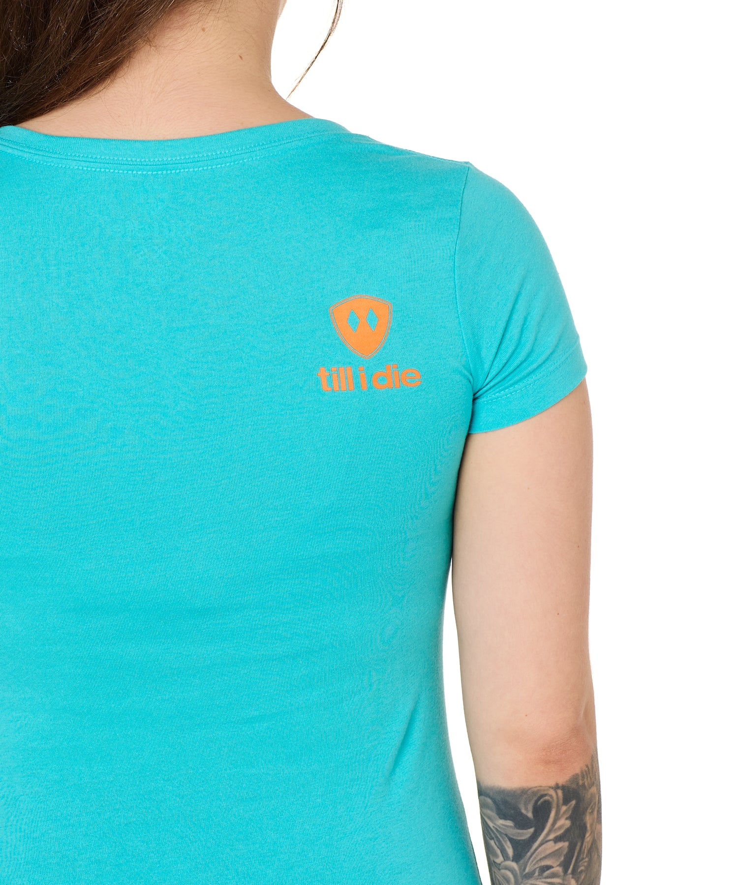 Back view of a female model wearing a Tahiti blue short sleeve shirt on a white background, featuring an orange Till I Die logo on the wearer’s top right shoulder.