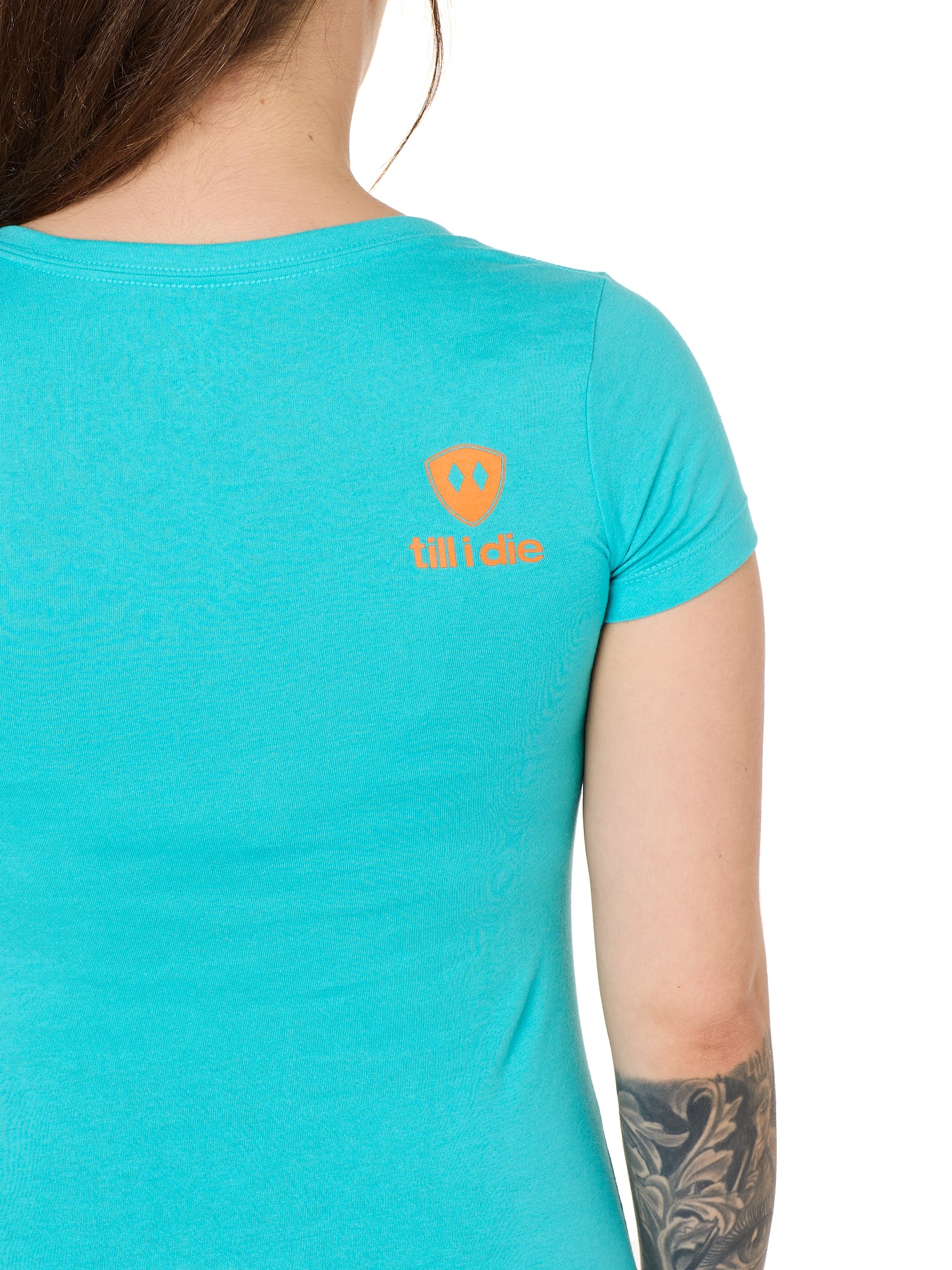 Back view of a female model wearing a Tahiti blue short sleeve shirt on a white background, featuring an orange Till I Die logo on the wearer’s top right shoulder.
