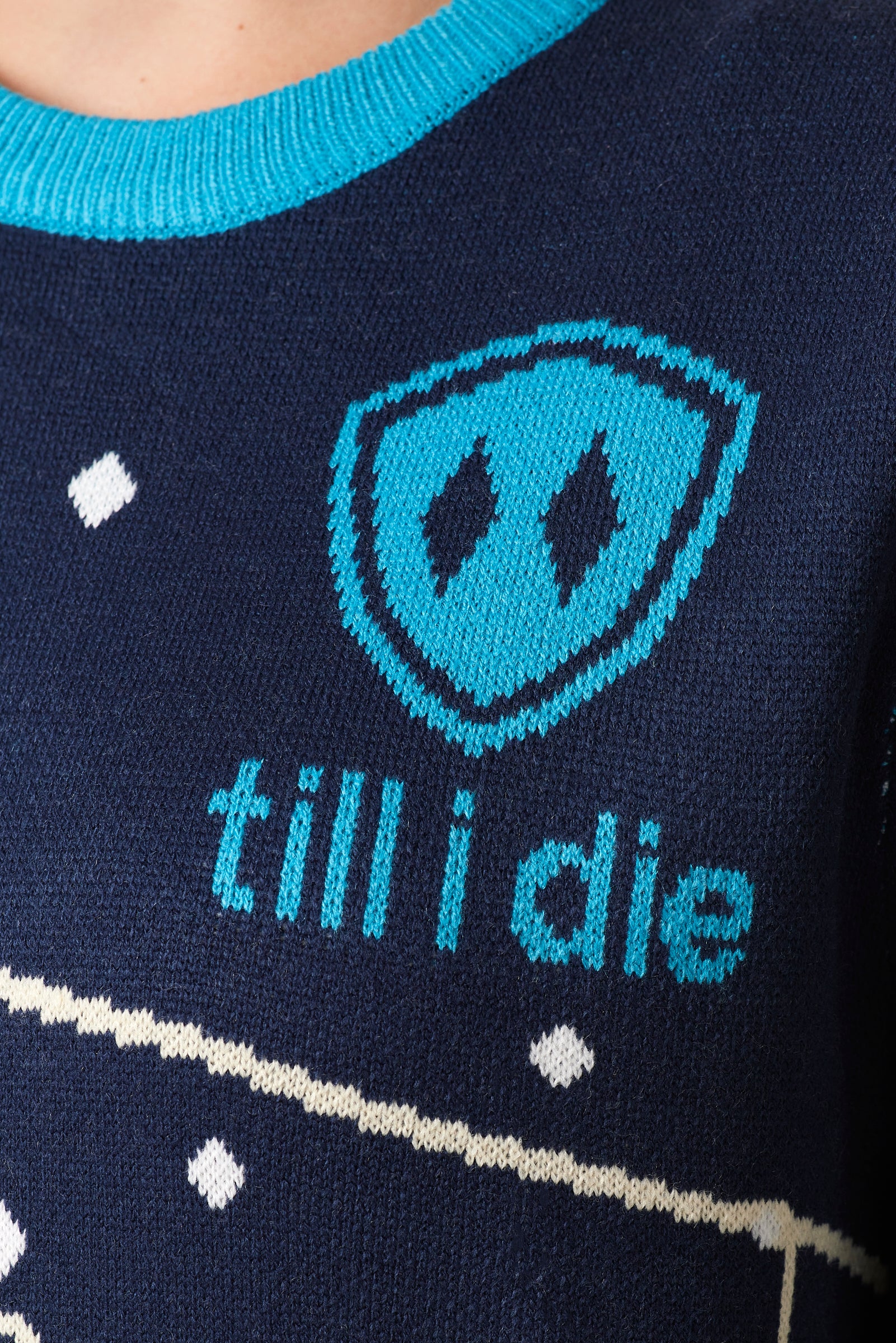 DETAIL OF A NAVY AND WHITE SWEATER FEATURING THE TILL I DIE SHIELD LOGO