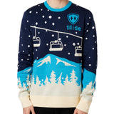 A male model wearing a blue and white 'Till I Die' brand pullover sweater with ski lift and mountain graphics.