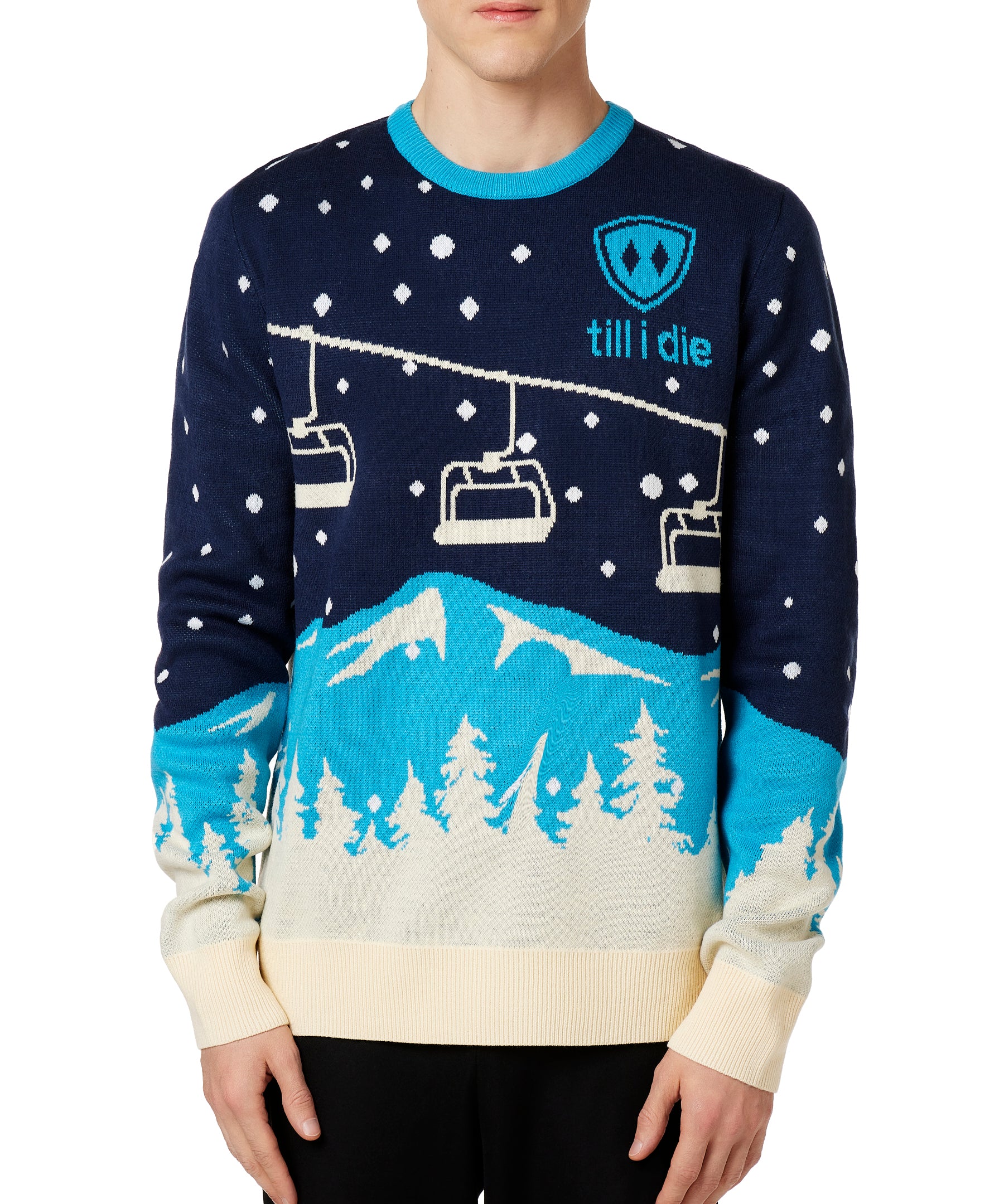 A male model wearing a blue and white 'Till I Die' brand pullover sweater with ski lift and mountain graphics.