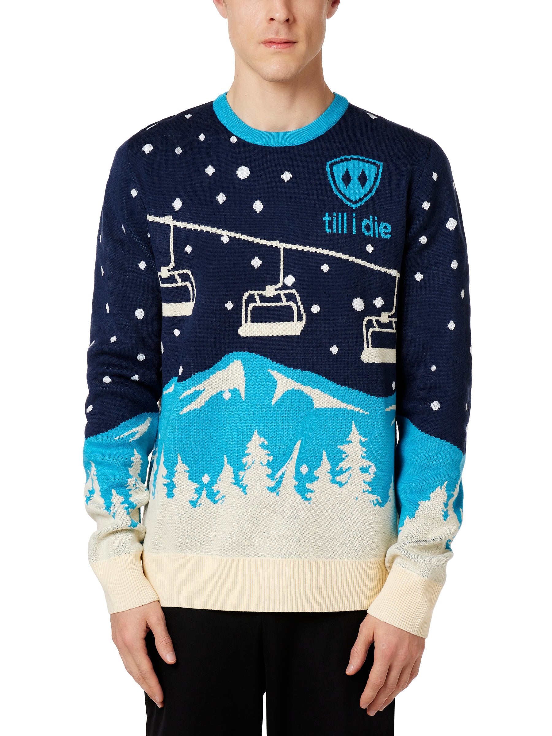 A male model wearing a blue and white 'Till I Die' brand pullover sweater with ski lift and mountain graphics.