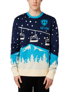 A male model wearing a blue and white 'Till I Die' brand pullover sweater with ski lift and mountain graphics.