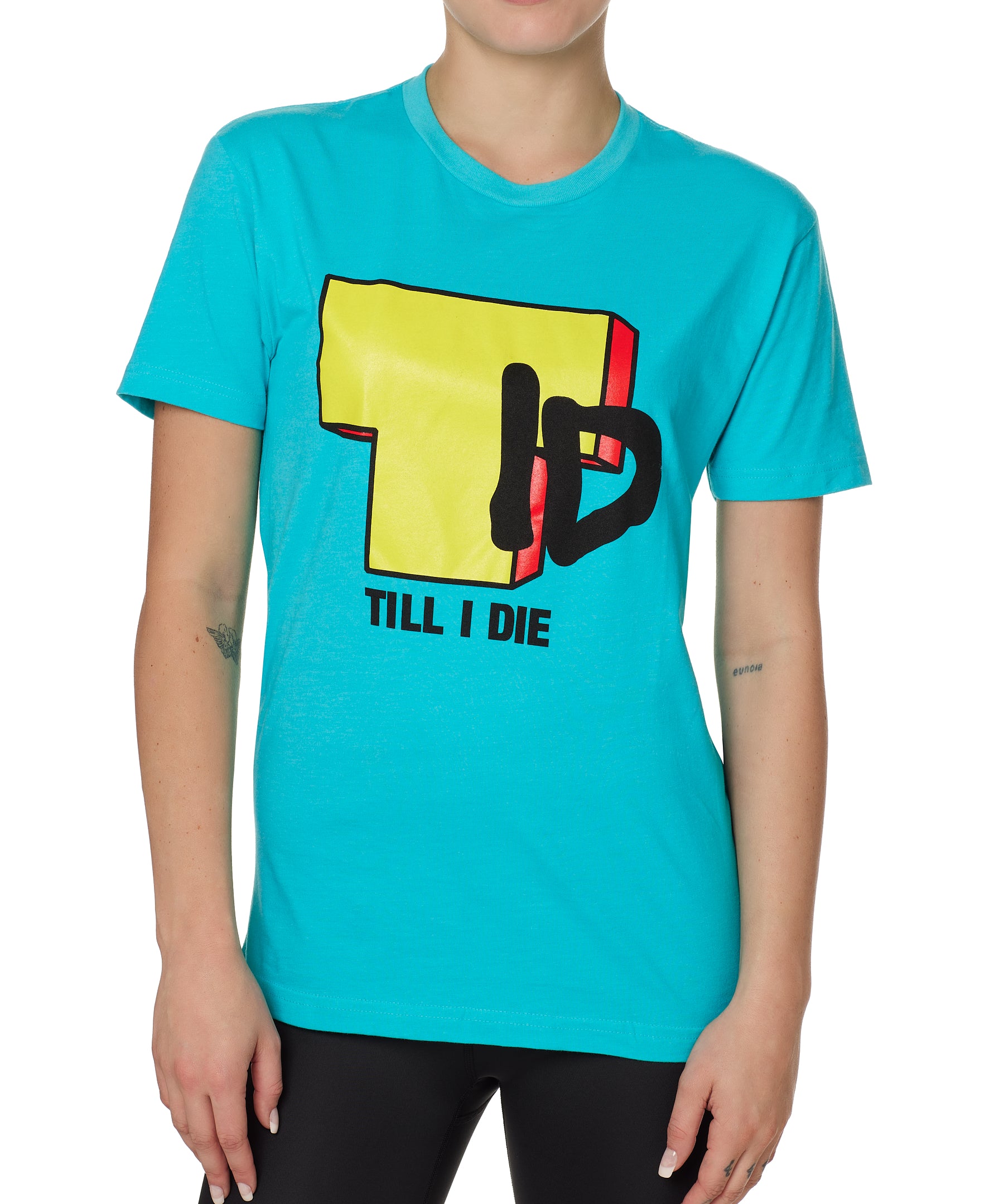 Front view of a female model wearing the TID TV crew neck tee in Tahiti Blue, displayed on a white background. The graphic features a large block-style yellow "T" alongside hand-drawn black "I" and "D" lettering, with "Till I Die" text beneath.