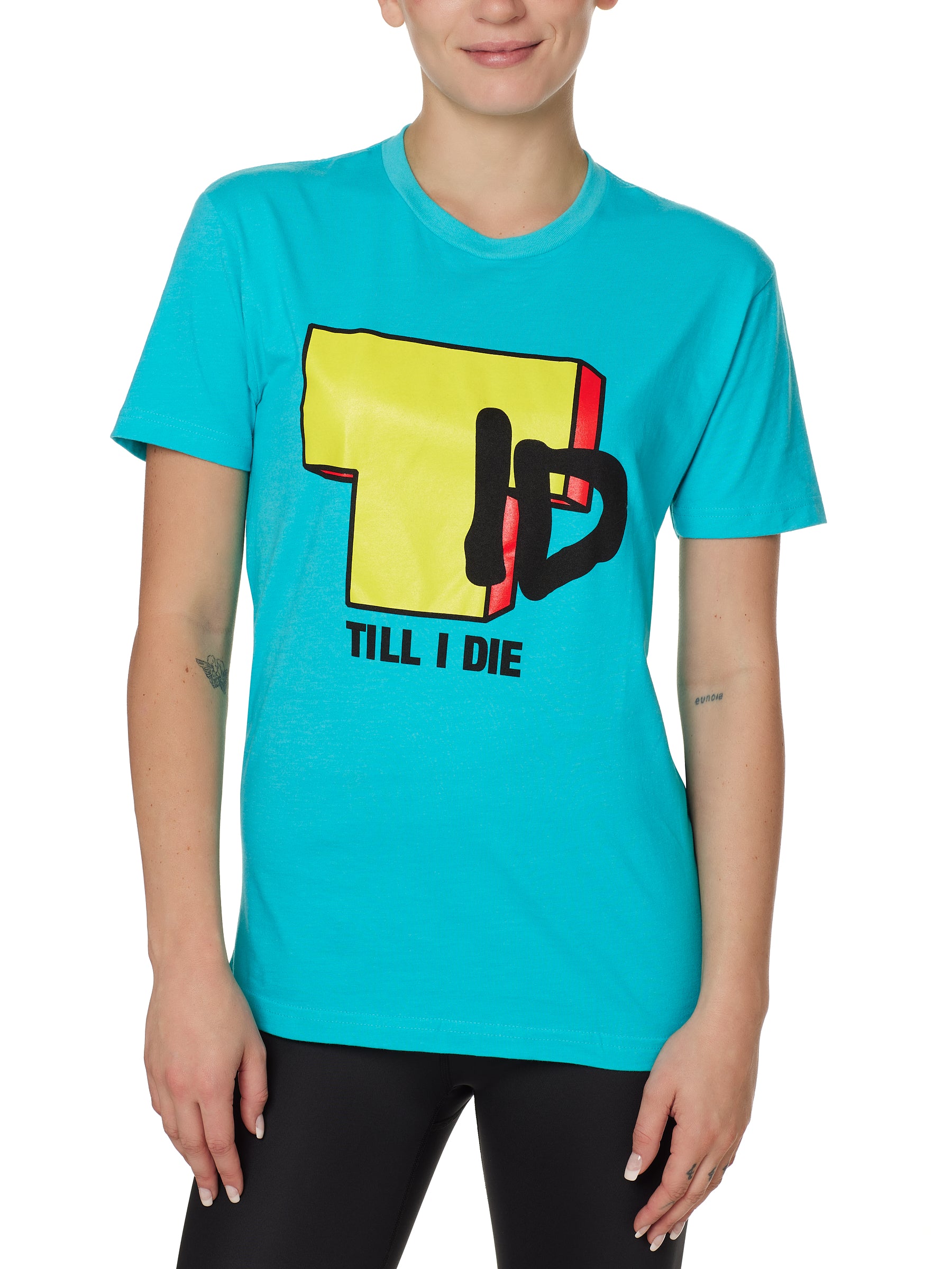 Front view of a female model wearing the TID TV crew neck tee in Tahiti Blue, displayed on a white background. The graphic features a large block-style yellow "T" alongside hand-drawn black "I" and "D" lettering, with "Till I Die" text beneath.