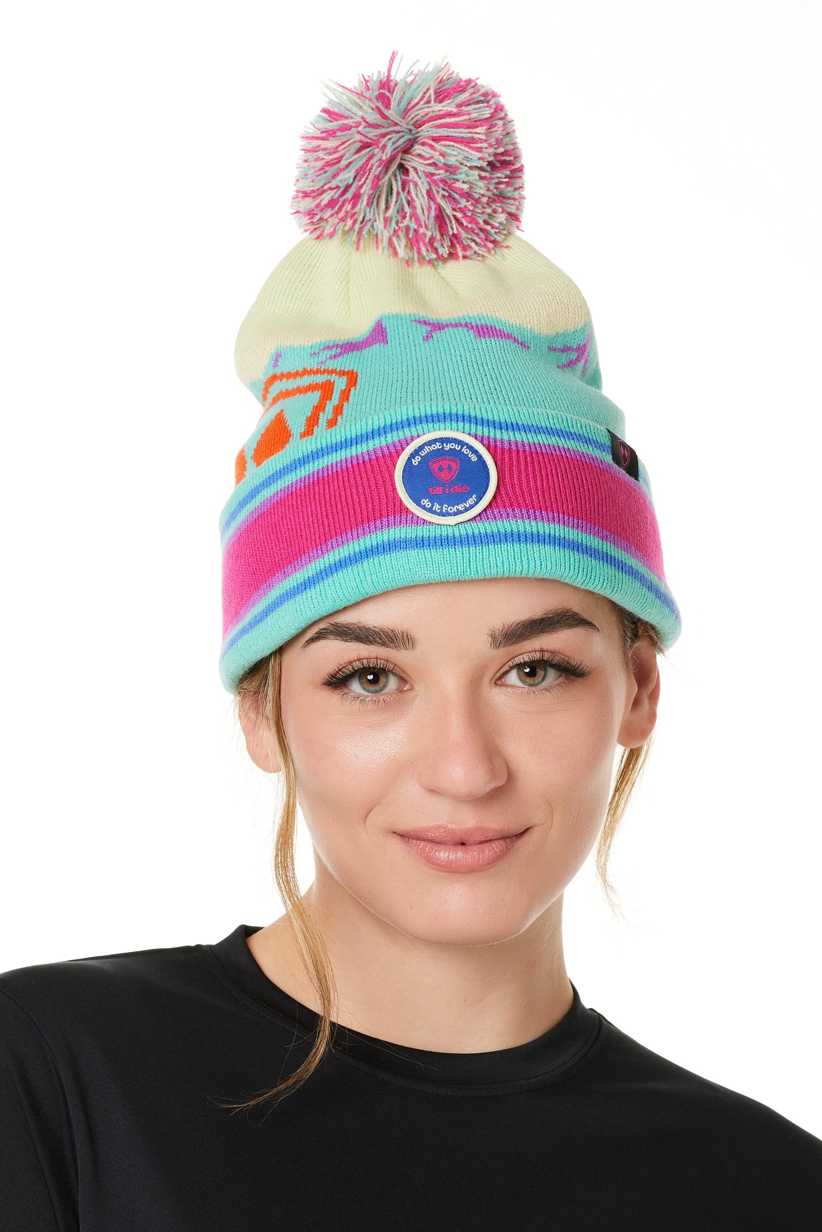 A WOMAN wearing a multicolored beanie with a pink pom-pom on top, featuring a TILL I DIE brand patch on the fold THAT SAYS "DO WHAT YOU LOVE. DO IT FOREVER."