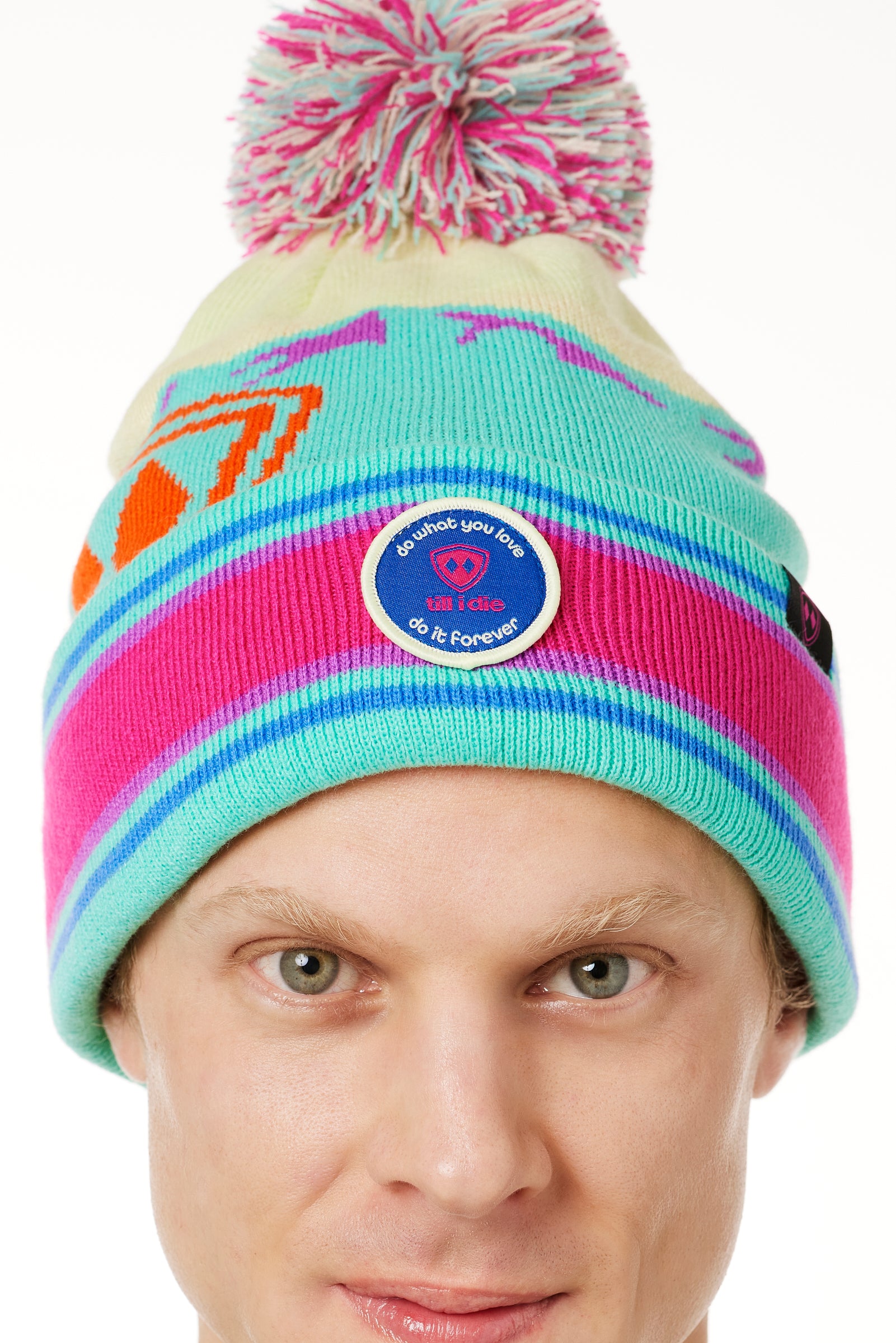 DETAIL A MAN wearing a multicolored beanie with a pink pom-pom on top, featuring a TILL I DIE brand patch on the fold THAT SAYS "DO WHAT YOU LOVE. DO IT FOREVER."