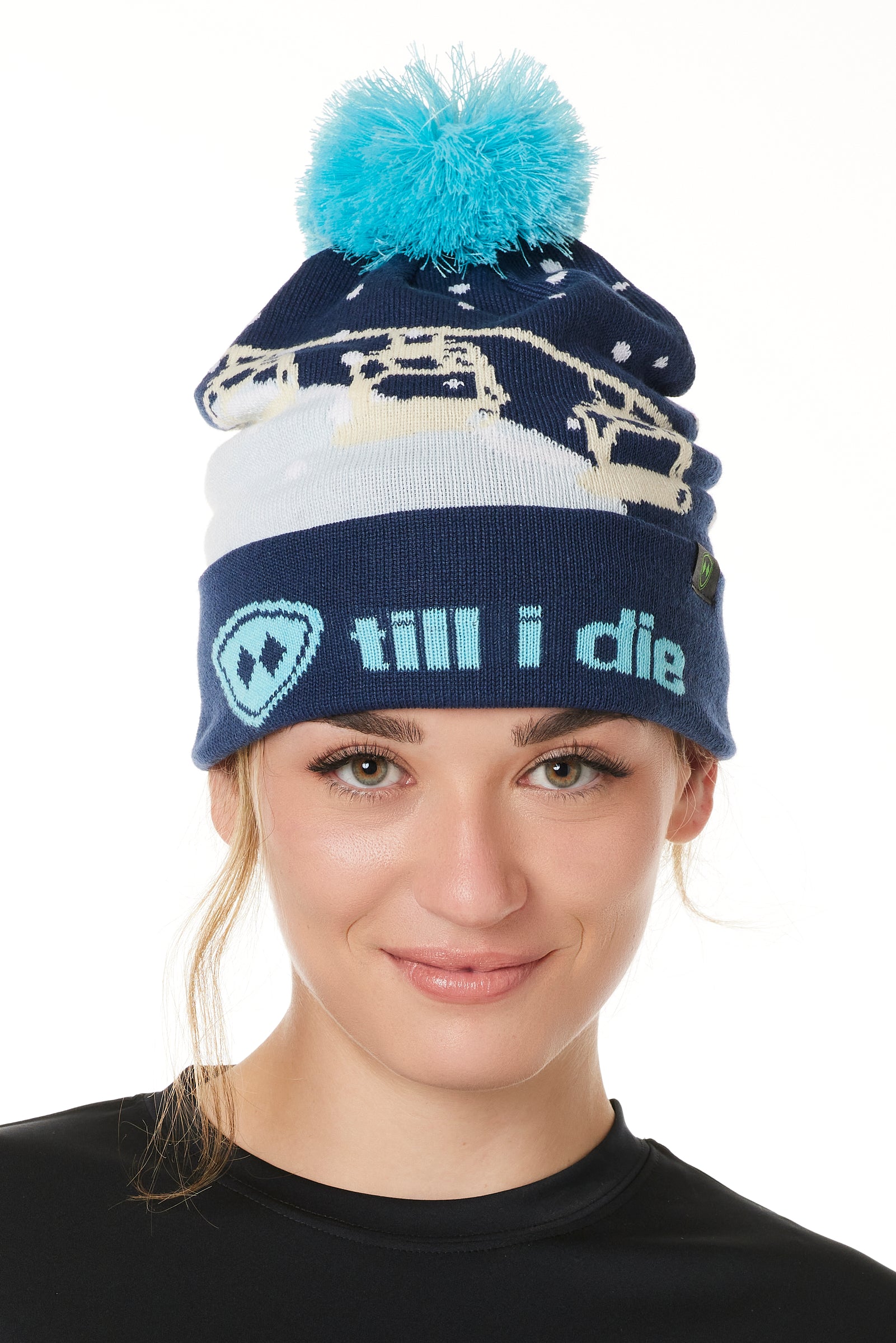 FEMALE MODEL WEARING A NAVY AND WHITE HAT WITH A BLUE POM POM AND CHAIRLIFT GRAPHIC WITH THE WORD "TILL I DIE" ON THE FOLD