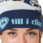 DETAIL OF A FEMALE MODEL WEARING A NAVY AND WHITE HAT WITH A BLUE POM POM AND CHAIRLIFT GRAPHIC WITH THE WORD "TILL I DIE" ON THE FOLD