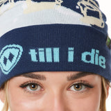 DETAIL OF A FEMALE MODEL WEARING A NAVY AND WHITE HAT WITH A BLUE POM POM AND CHAIRLIFT GRAPHIC WITH THE WORD "TILL I DIE" ON THE FOLD