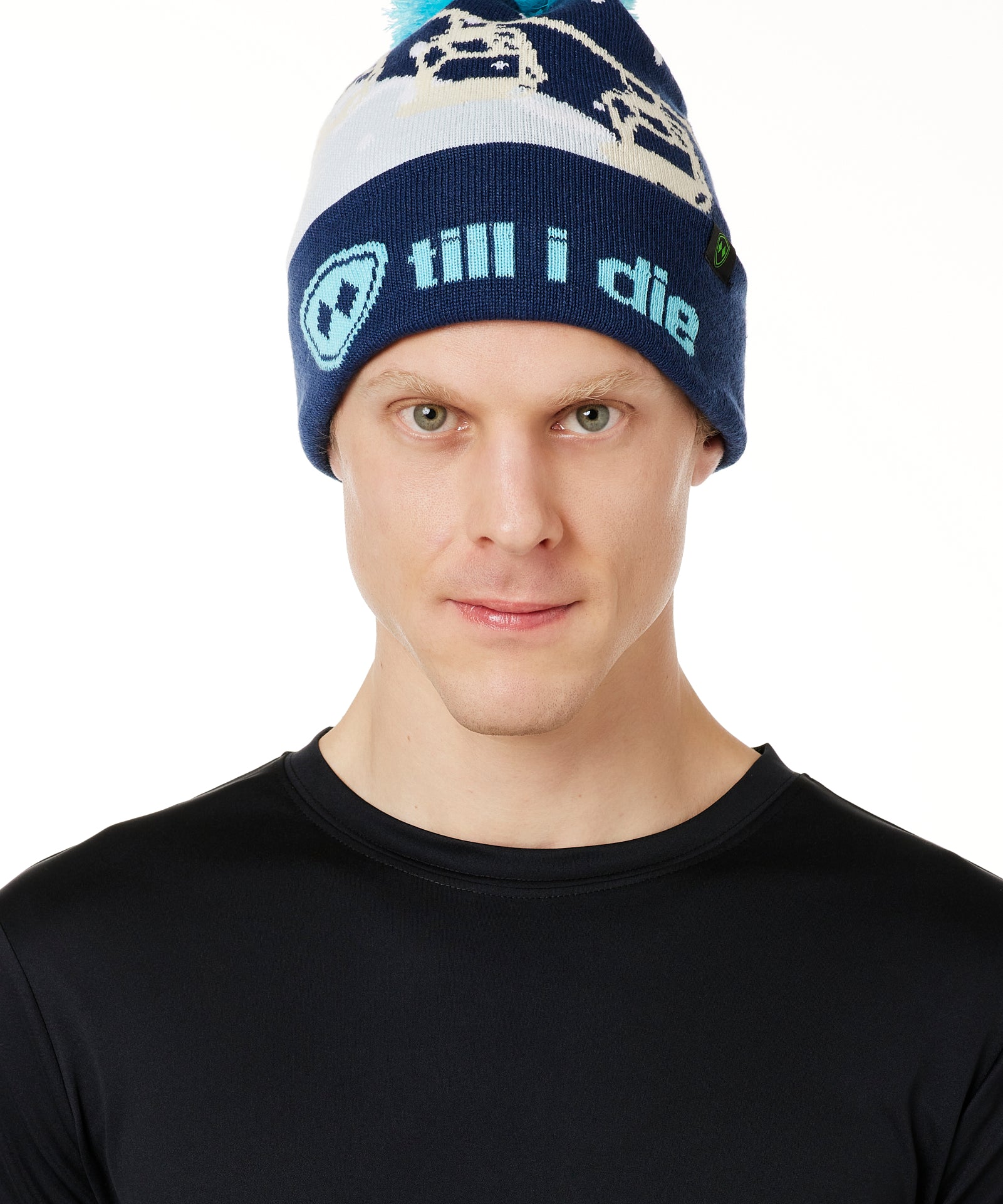 MALE MODEL WEARING A NAVY AND WHITE HAT WITH A BLUE POM POM AND CHAIRLIFT GRAPHIC WITH THE WORD "TILL I DIE" ON THE FOLD