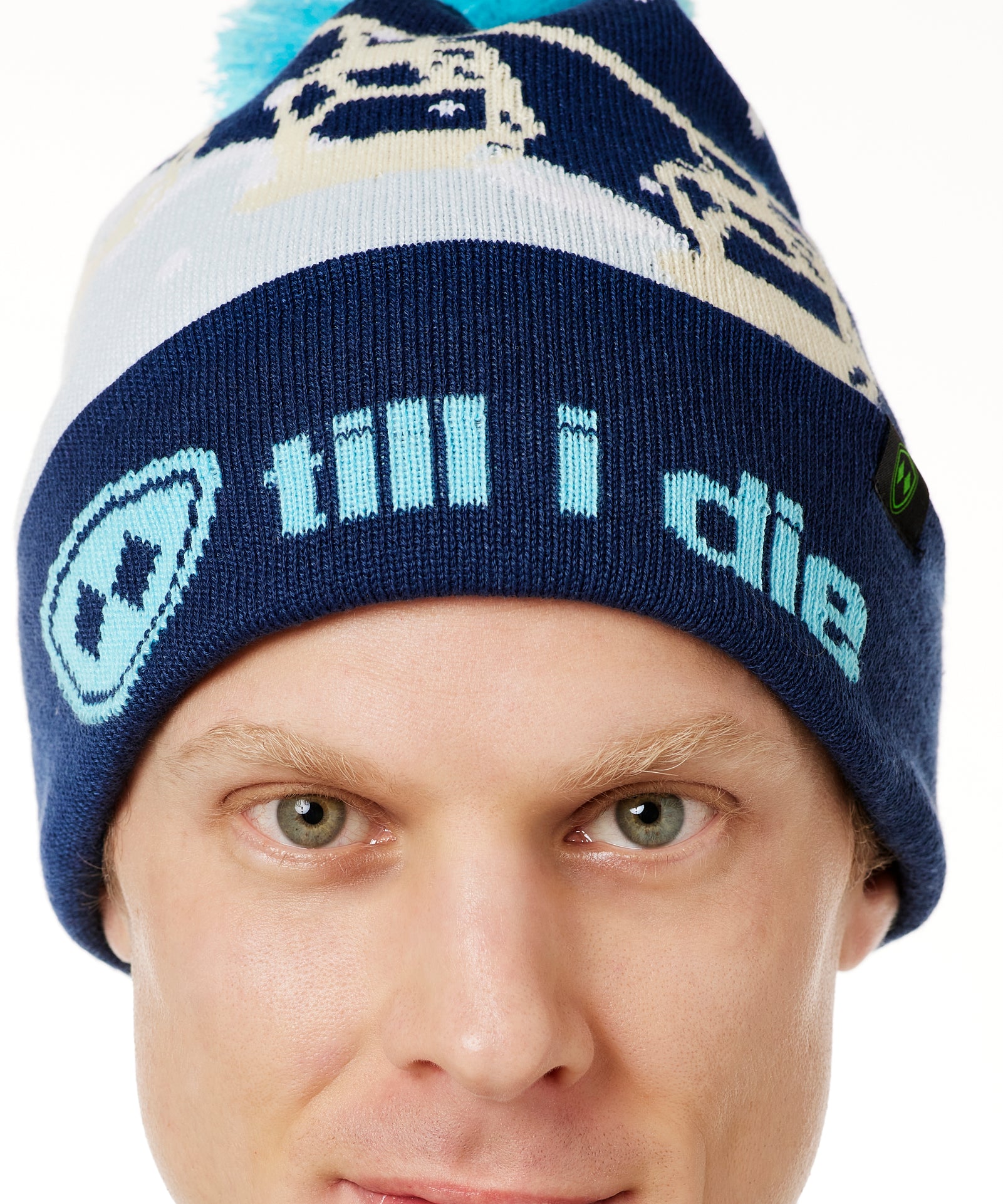 DETAIL OF A MALE MODEL WEARING A NAVY AND WHITE HAT WITH A BLUE POM POM AND CHAIRLIFT GRAPHIC WITH THE WORD "TILL I DIE" ON THE FOLD