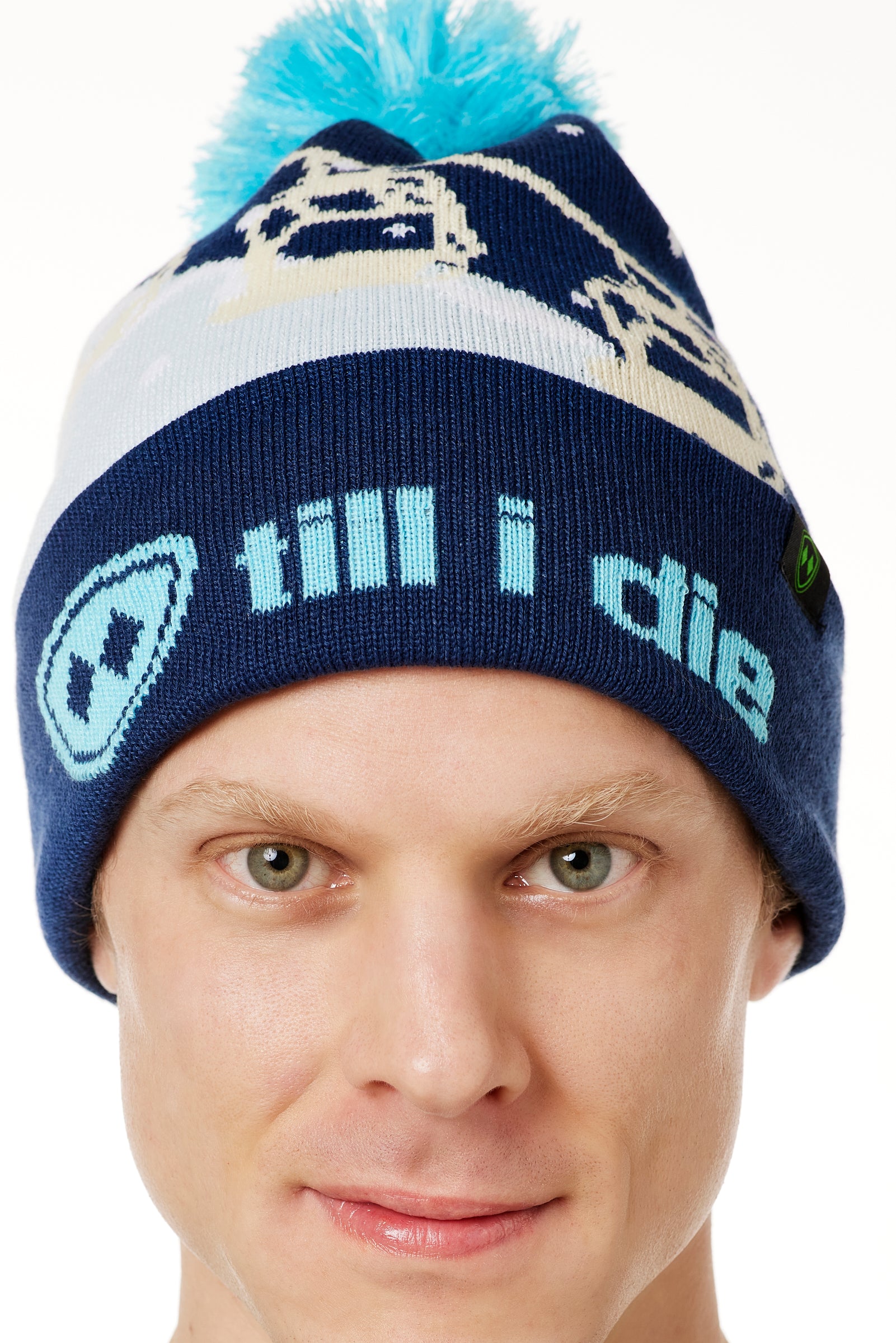 DETAIL OF A MALE MODEL WEARING A NAVY AND WHITE HAT WITH A BLUE POM POM AND CHAIRLIFT GRAPHIC WITH THE WORD "TILL I DIE" ON THE FOLD