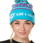 FEMALE MODEL WEARING A TEAL AND PINK HAT WITH A POM POM AND THE WORDS "APRES SKI"