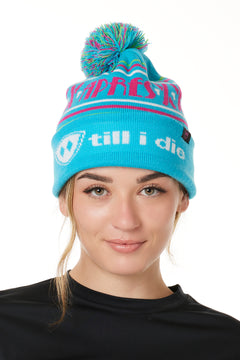 FEMALE MODEL WEARING A TEAL AND PINK HAT WITH A POM POM AND THE WORDS "APRES SKI"