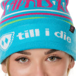 DETAIL OF A FEMALE MODEL WEARING A TEAL AND PINK HAT WITH A POM POM AND THE WORDS "APRES SKI"
