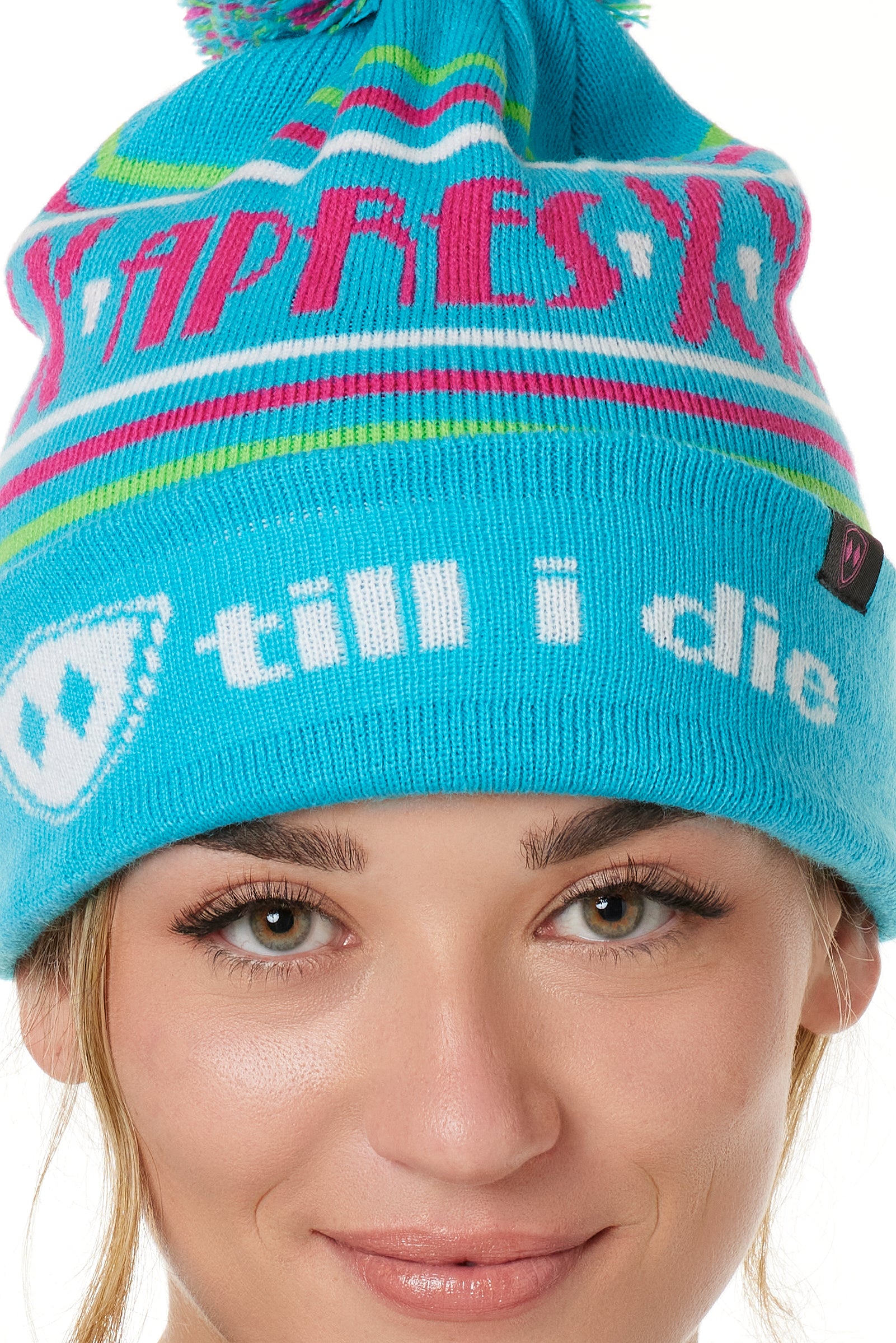DETAIL OF A FEMALE MODEL WEARING A TEAL AND PINK HAT WITH A POM POM AND THE WORDS "APRES SKI"