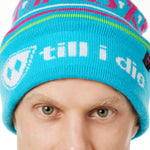 DETAIL OF A MALE MODEL WEARING A TEAL AND PINK HAT WITH A POM POM AND THE WORDS "APRES SKI"