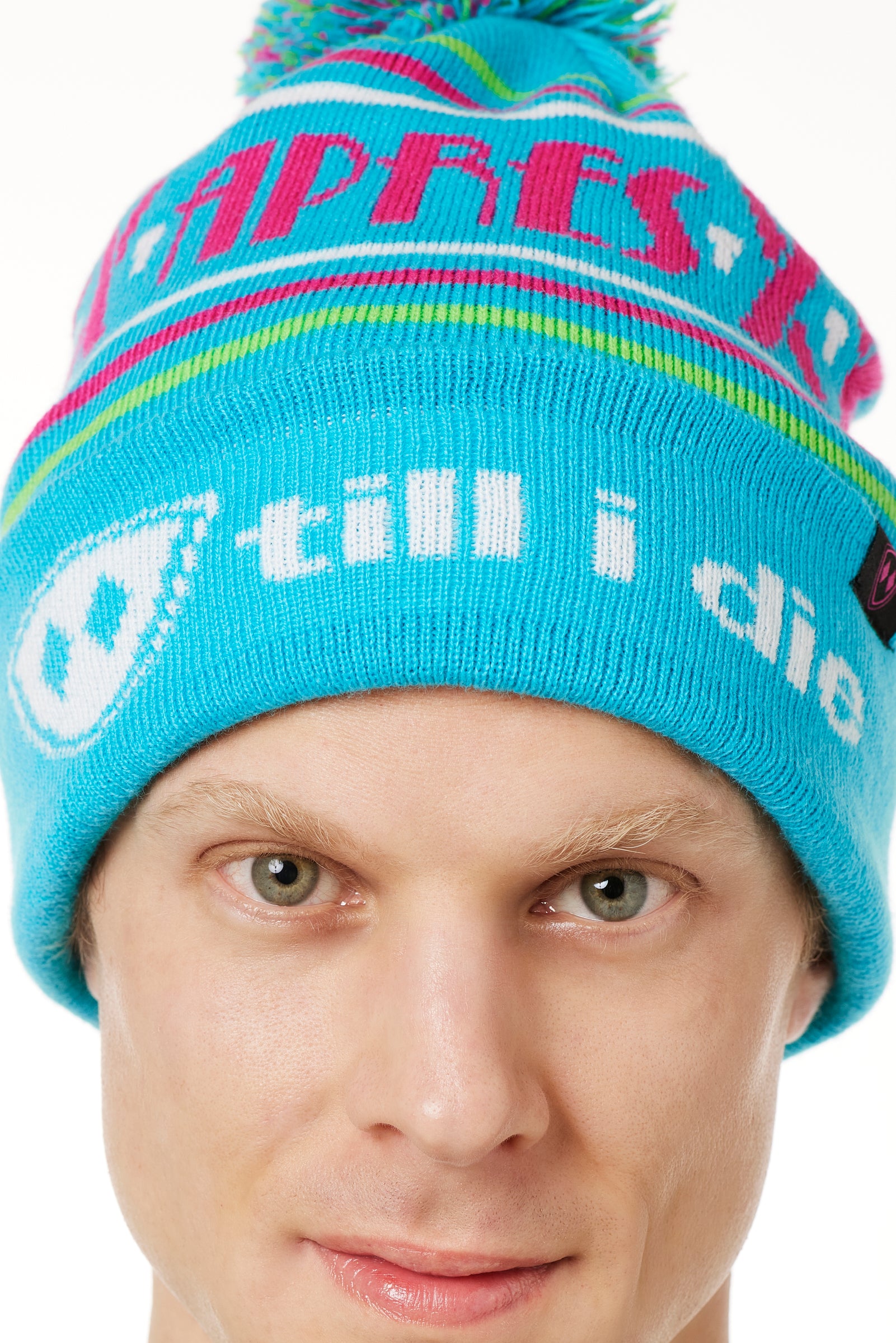 DETAIL OF A MALE MODEL WEARING A TEAL AND PINK HAT WITH A POM POM AND THE WORDS "APRES SKI"