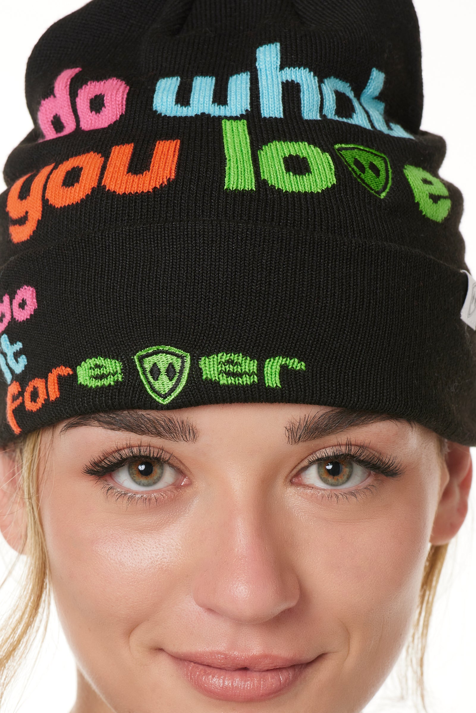 DETAIL OF A FEMALE MODEL WEARING A BLACK BEANIE WITH MULTICOLORED WORDS SAYING "DO WHAT YOU LOVE. DO IT FOREVER" 