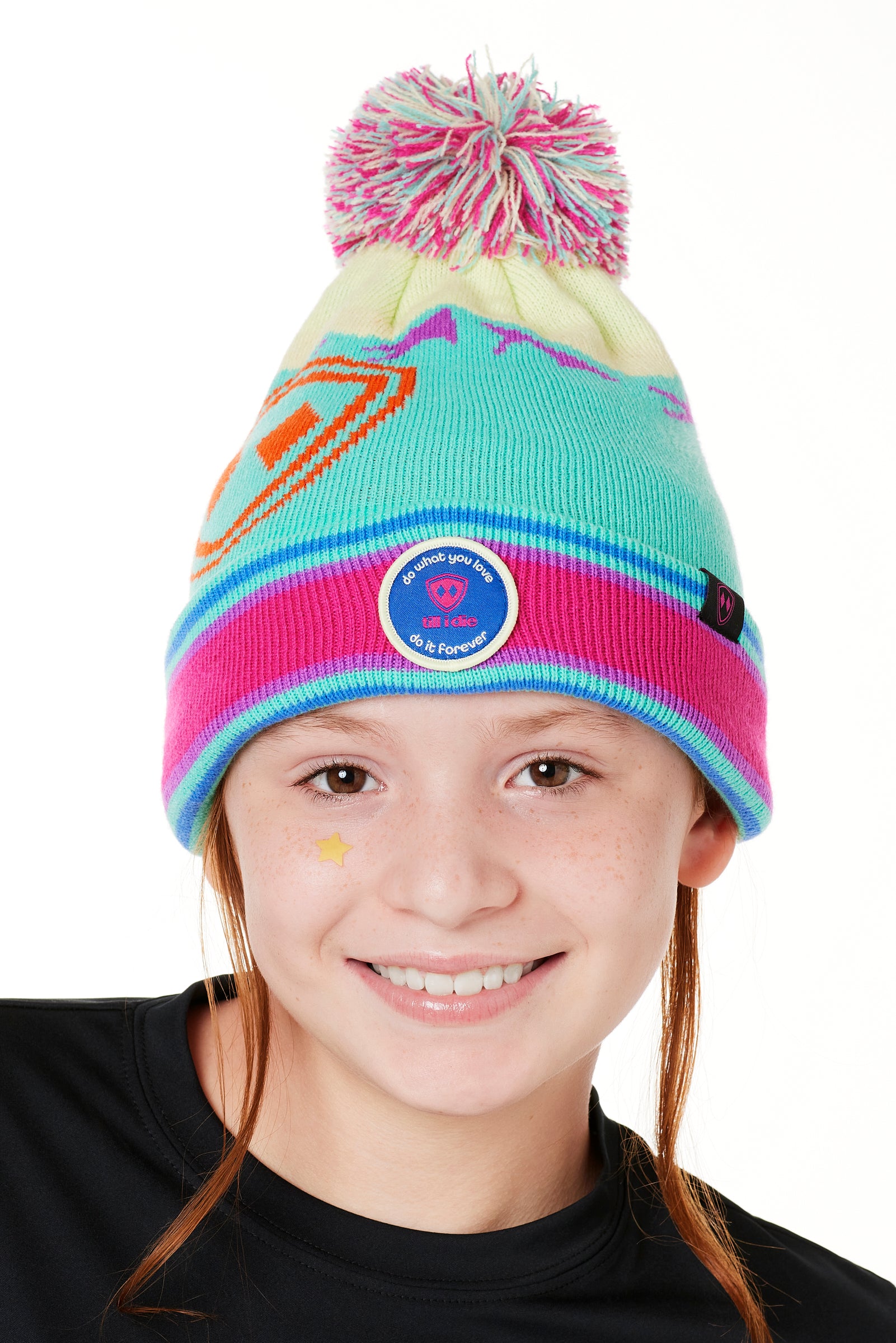 A YOUTH wearing a multicolored beanie with a pink pom-pom on top, featuring a TILL I DIE brand patch on the fold THAT SAYS "DO WHAT YOU LOVE. DO IT FOREVER."