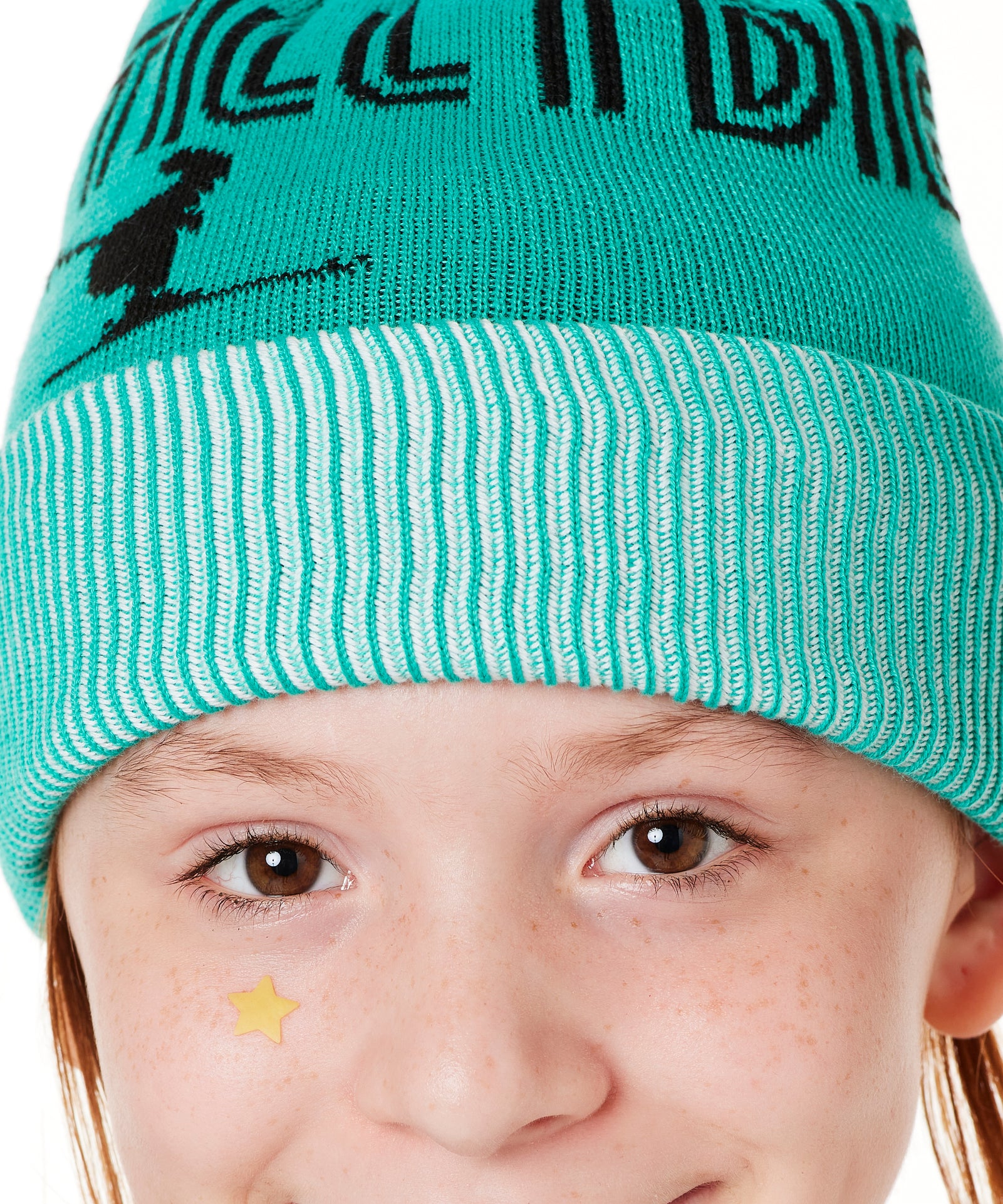 DETAIL OF A YOUTH MODEL  WEARING A MINT GREEN BEANIE WITH A WHITE POM POM AND THE GRAPHIC OF A SKIER