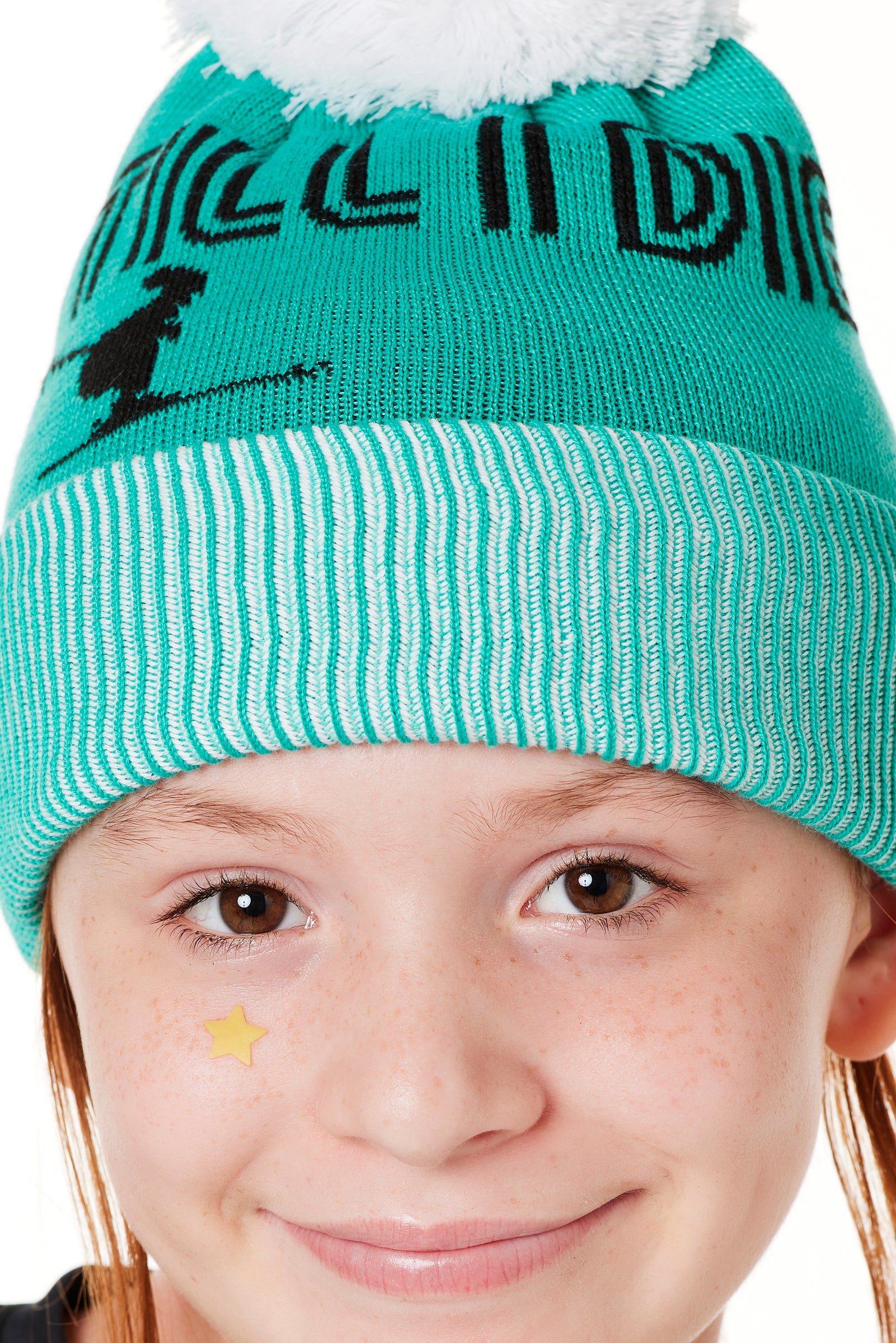 DETAIL OF A YOUTH MODEL  WEARING A MINT GREEN BEANIE WITH A WHITE POM POM AND THE GRAPHIC OF A SKIER