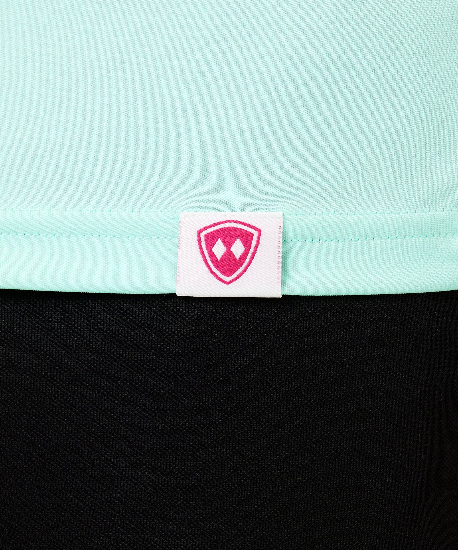 DETAIL OF A MINT GREEN LONG SLEEVE BASE LAYER WITH THE TILL I DIE SHIELD LOGO WOVEN LABEL ON THE HEM