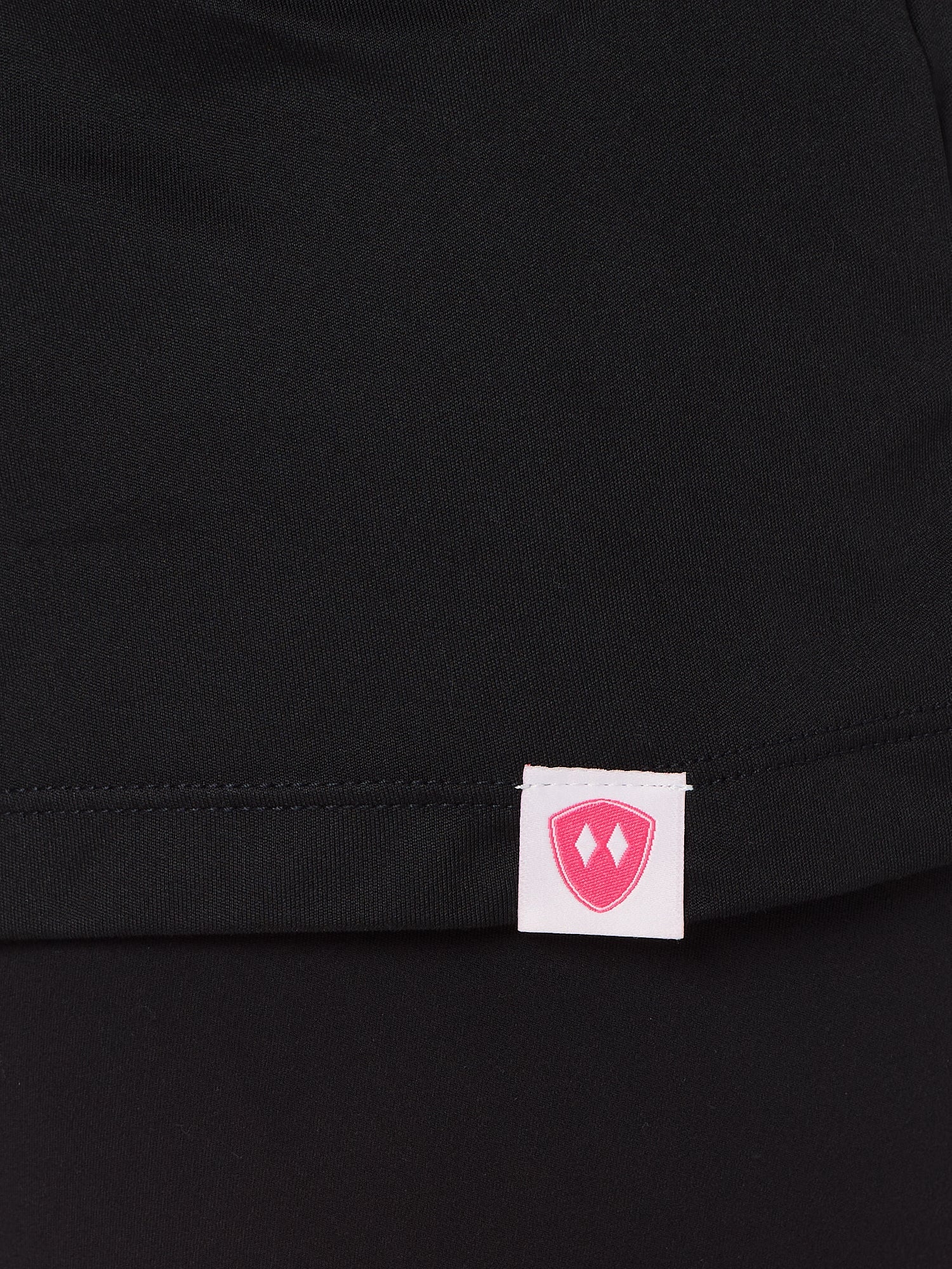 Close-up detail of a pink Double Diamond Shield woven hem label on a black performance long sleeve shirt.