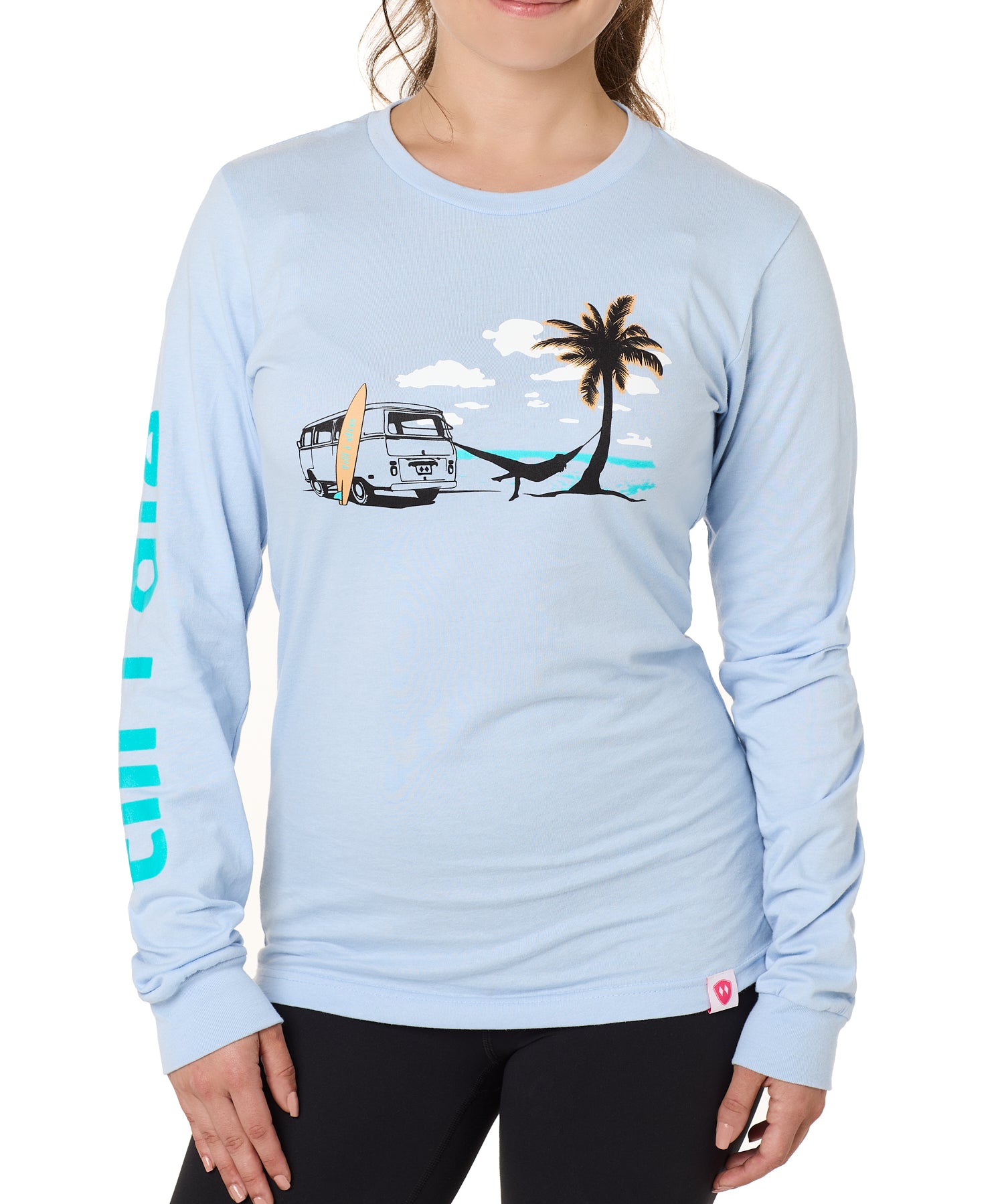 Front view of a female model wearing the Hammock long sleeve tee in light blue, displayed on a white background. The graphic depicts a vintage VW bus parked on a beach, with a surfboard leaning against it and a silhouetted figure relaxing in a hammock strung between the van and a palm tree.